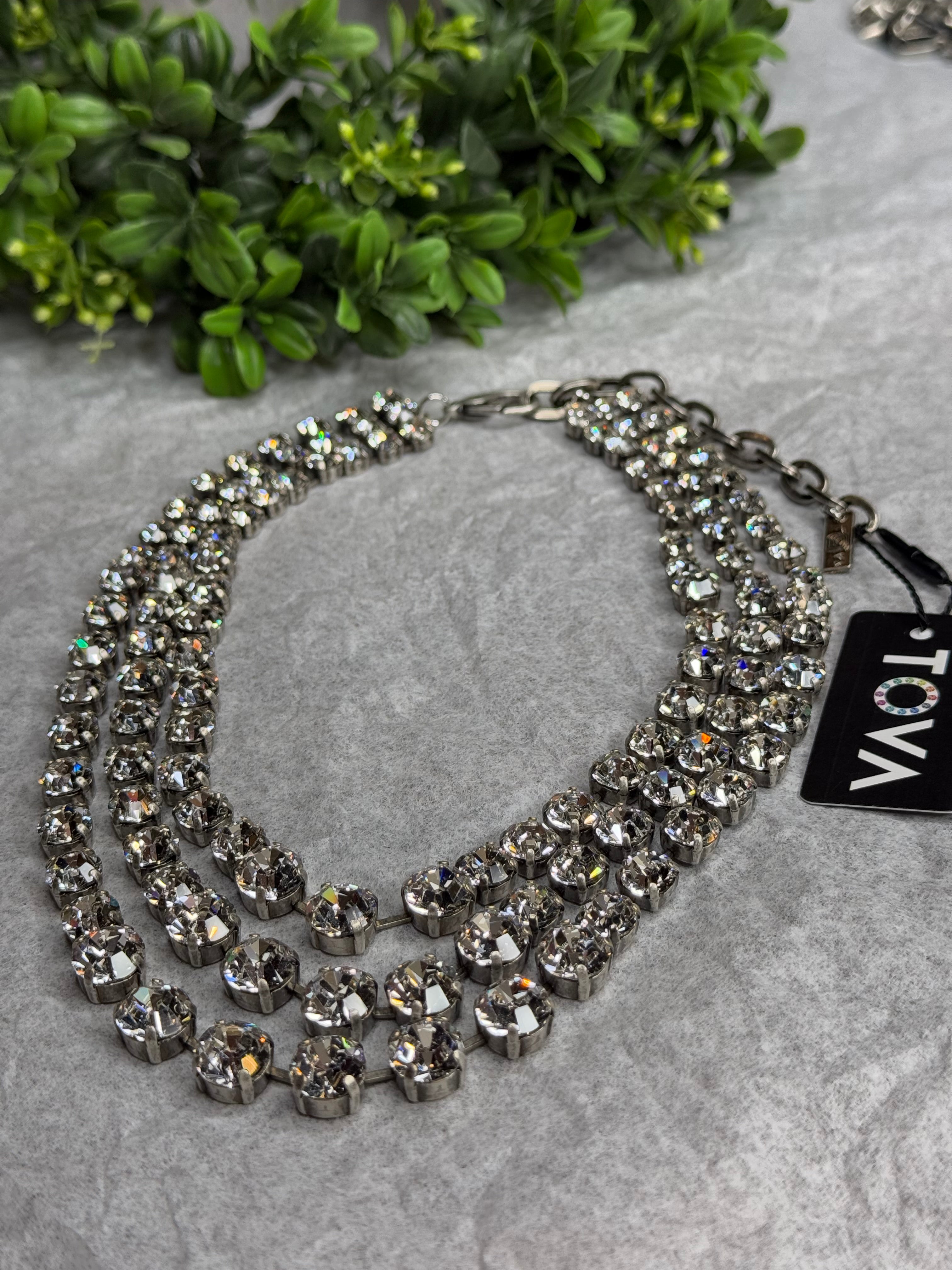 Silver necklace with crystals on a gray surface with greenery