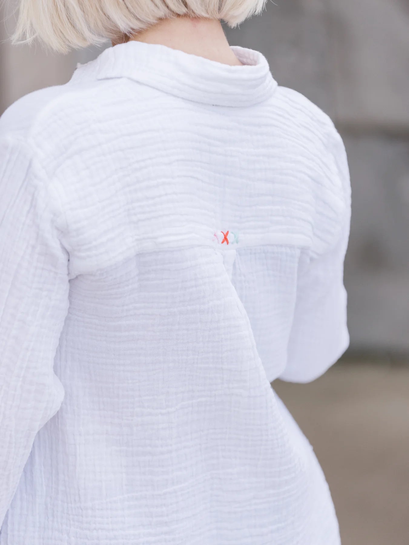 Back view of model wearing Abby Cotton Gauze Button Up Shirt. Detail of X-Stitching along top yoke of shirt.