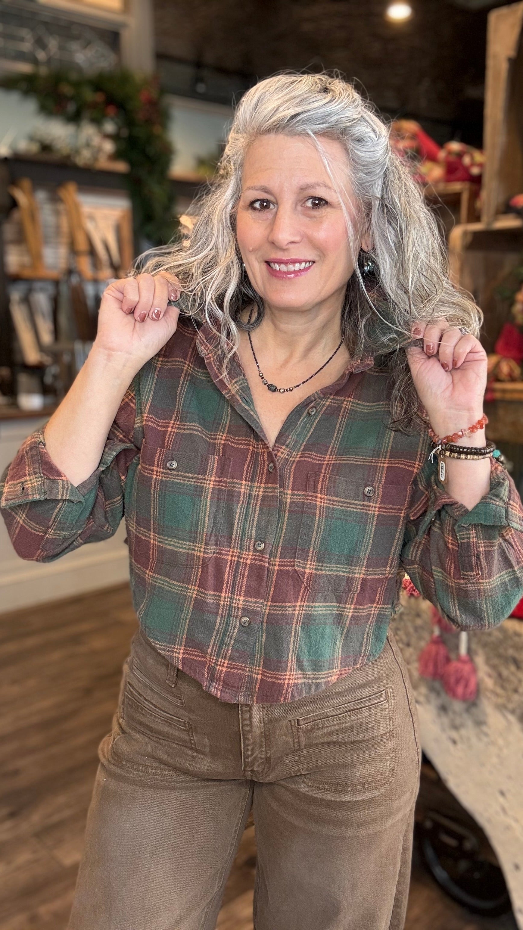 Woman wearing a Green plaid crop flannel shirt and brown barrel jeans in a store setting.