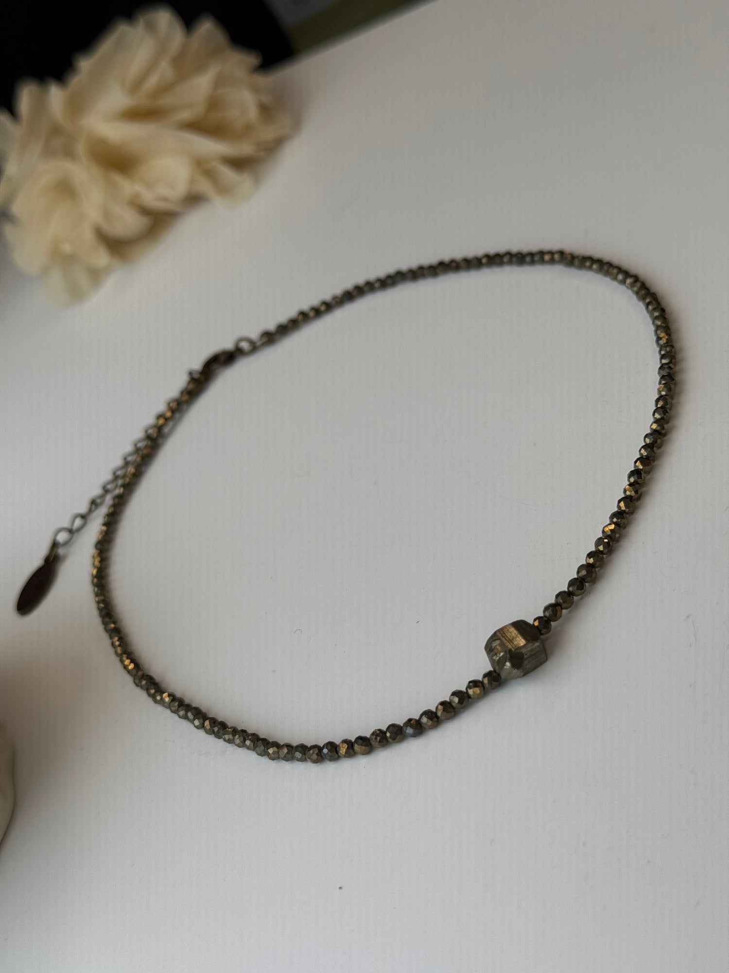 Beaded necklace on a white surface with a blurred flower in the background
