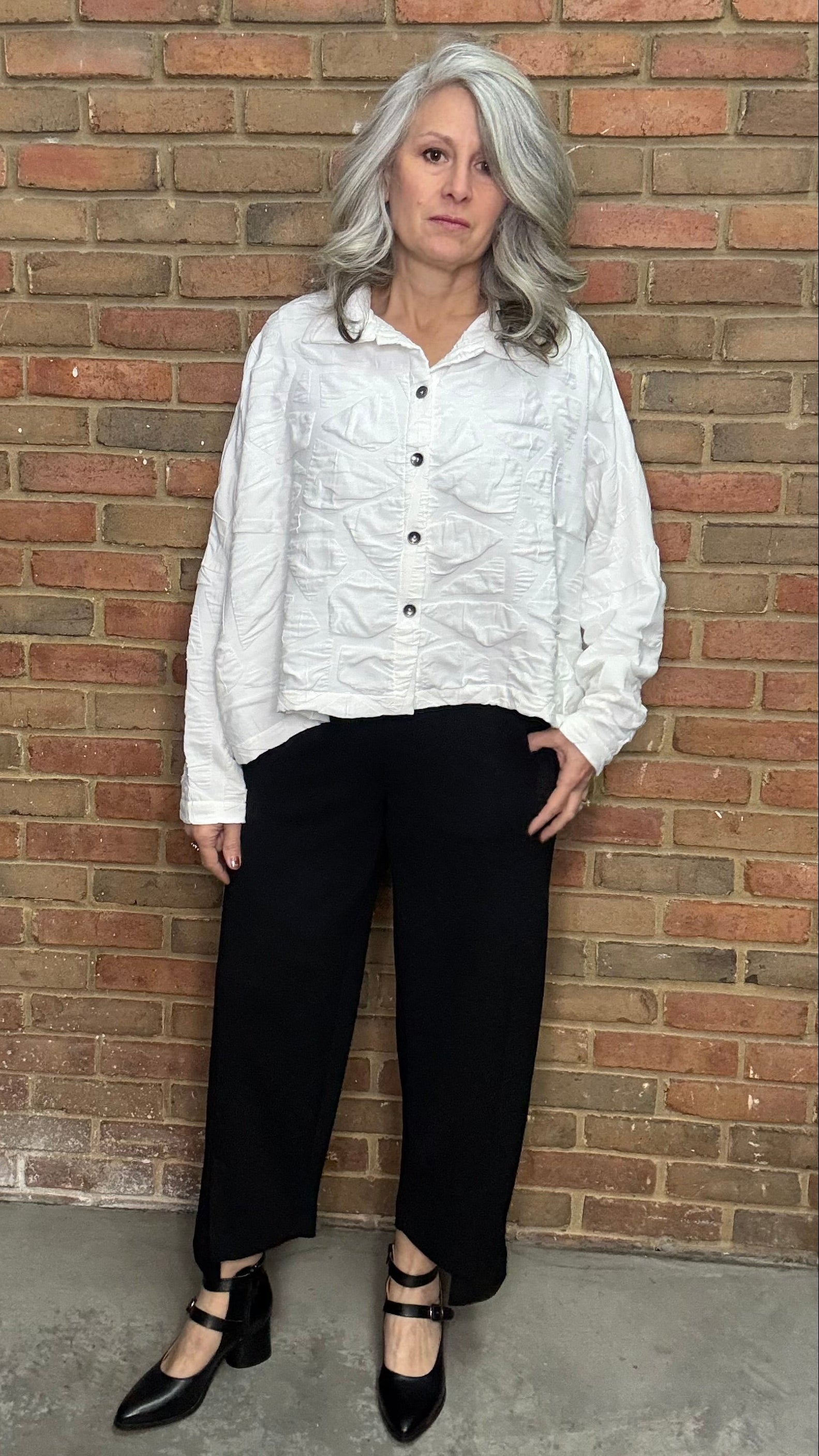 Person wearing a white shirt and black pants against a brick wall