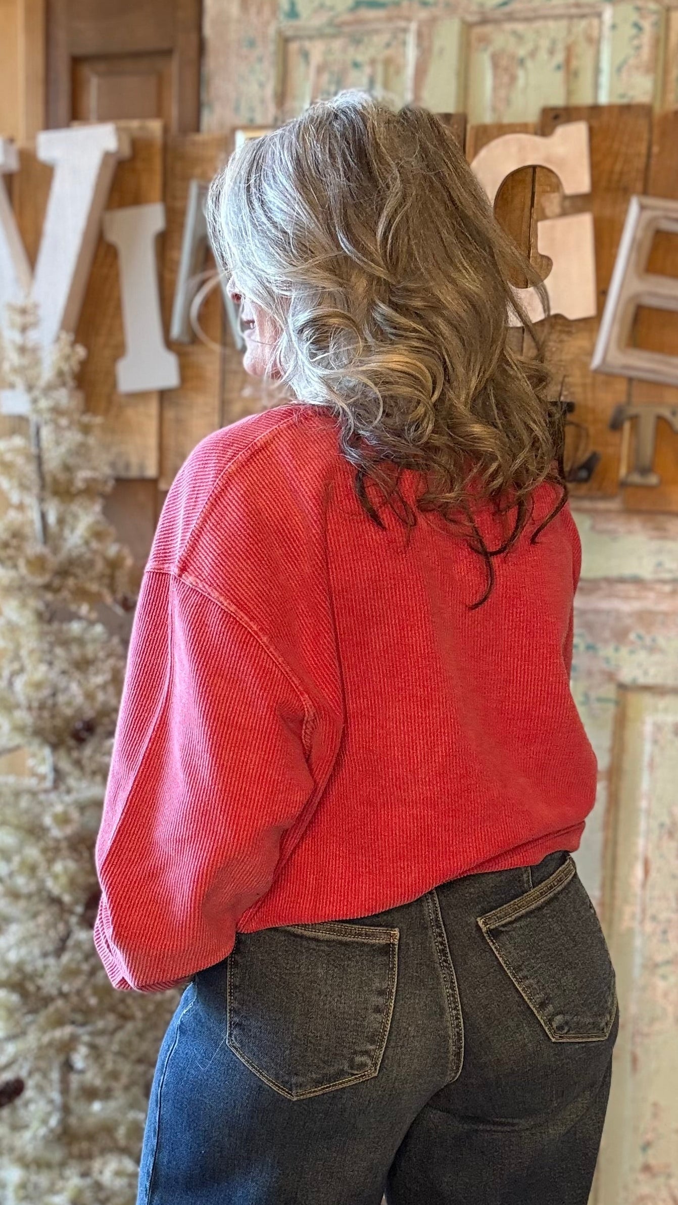 Person wearing a red shirt and blue jeans standing in front of decorative wall.