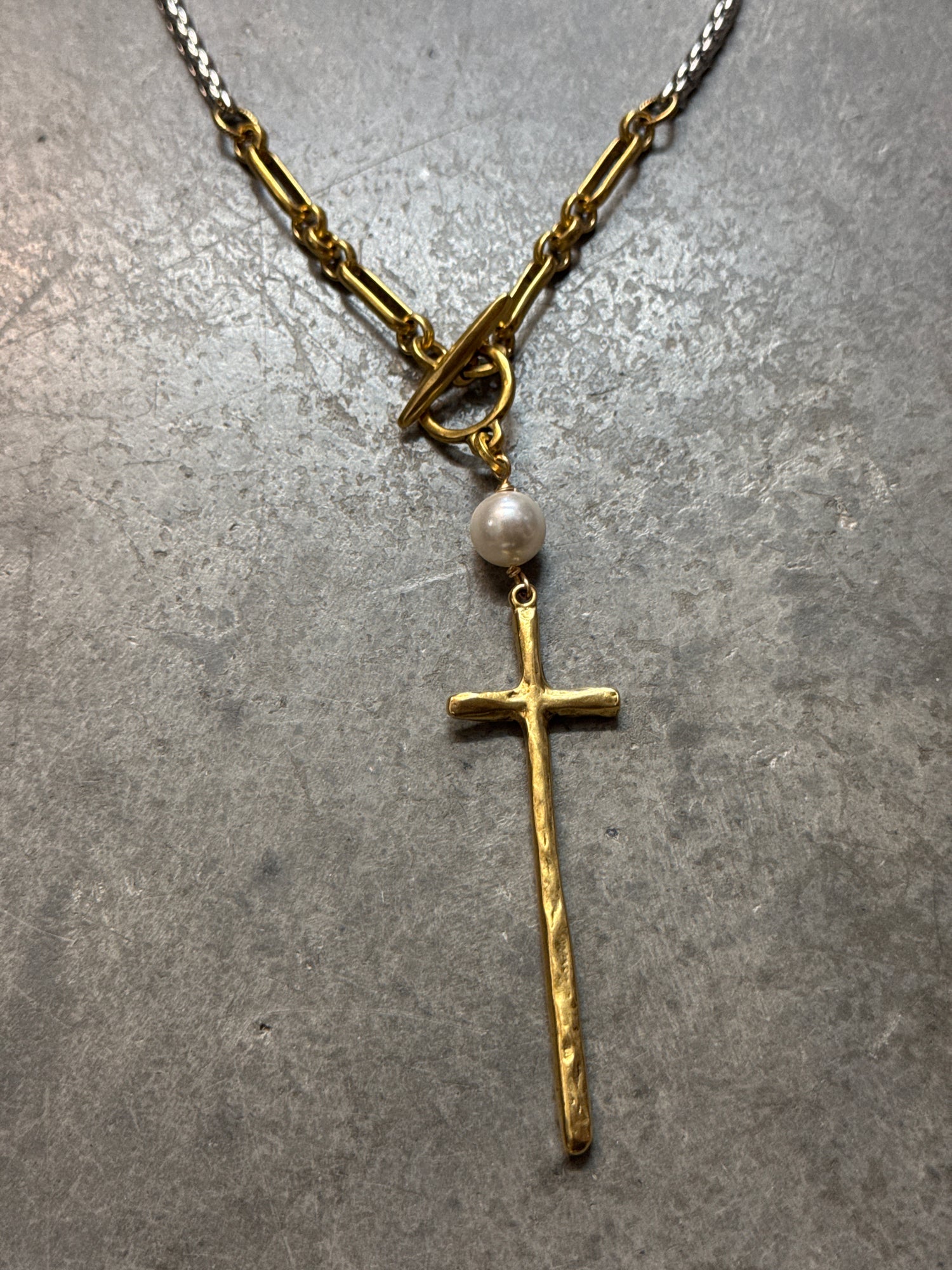 Gold cross necklace with a pearl on a gray surface