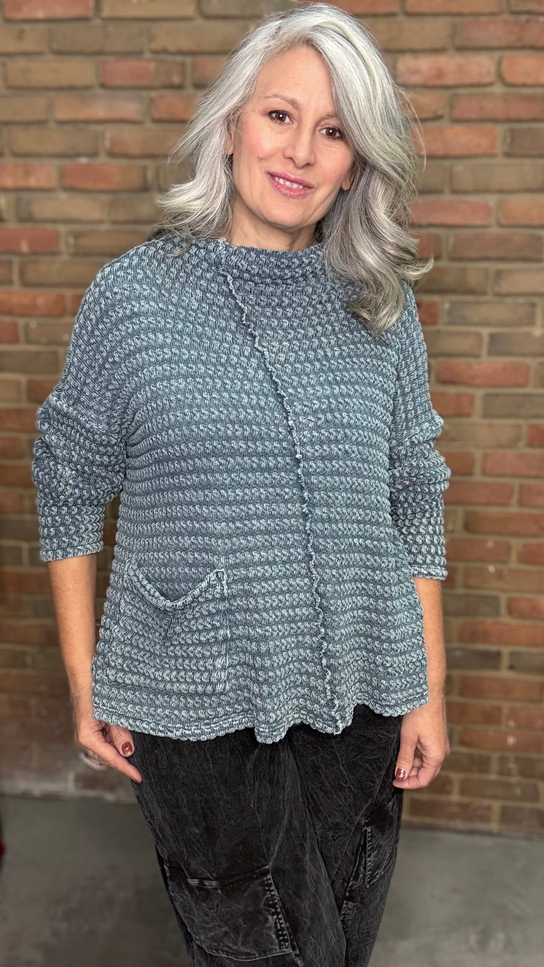 Woman wearing a textured blue sweater against a brick wall.