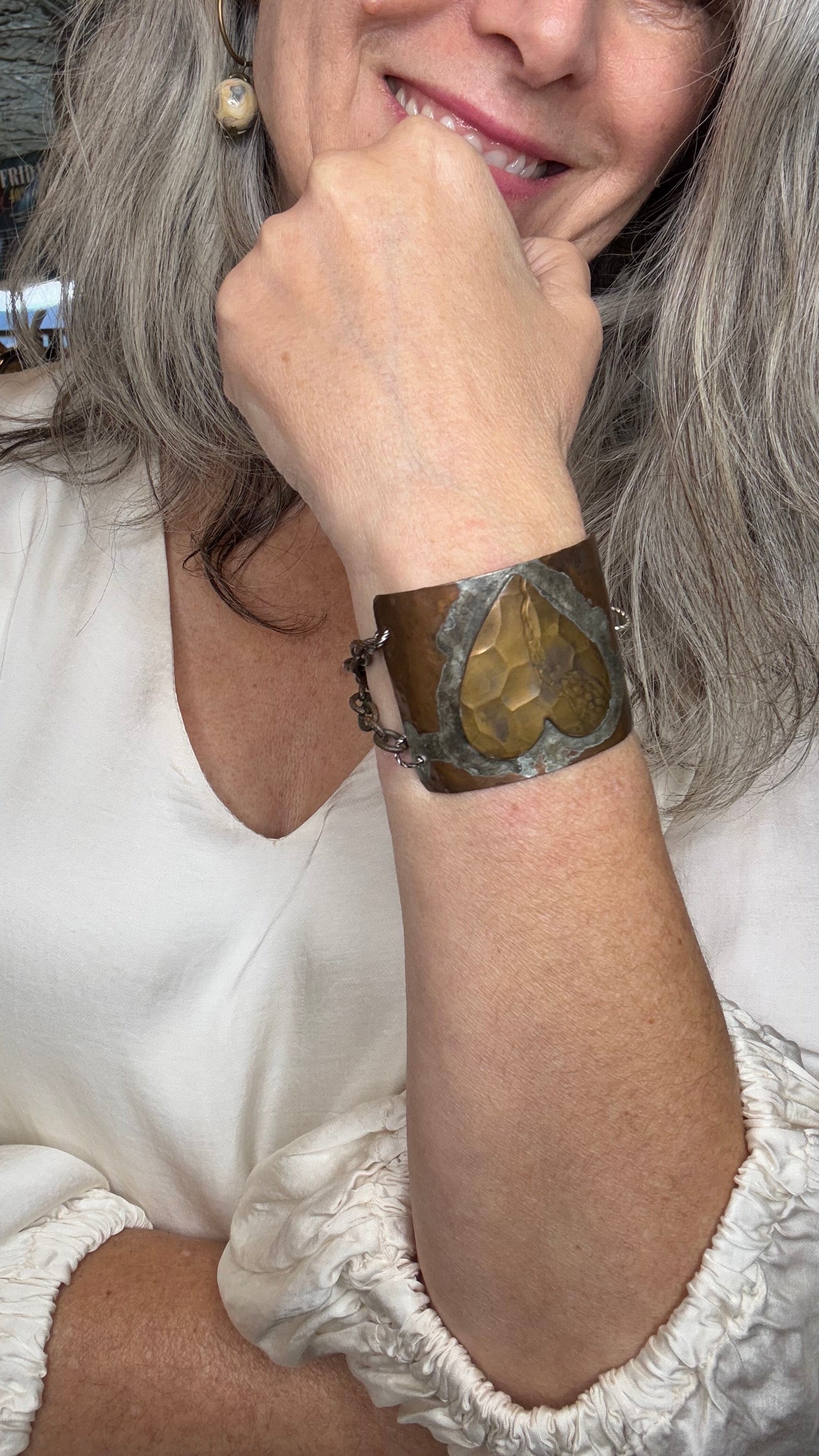 Person wearing a white dress with lace details and a metal half cuff with heart wristband.