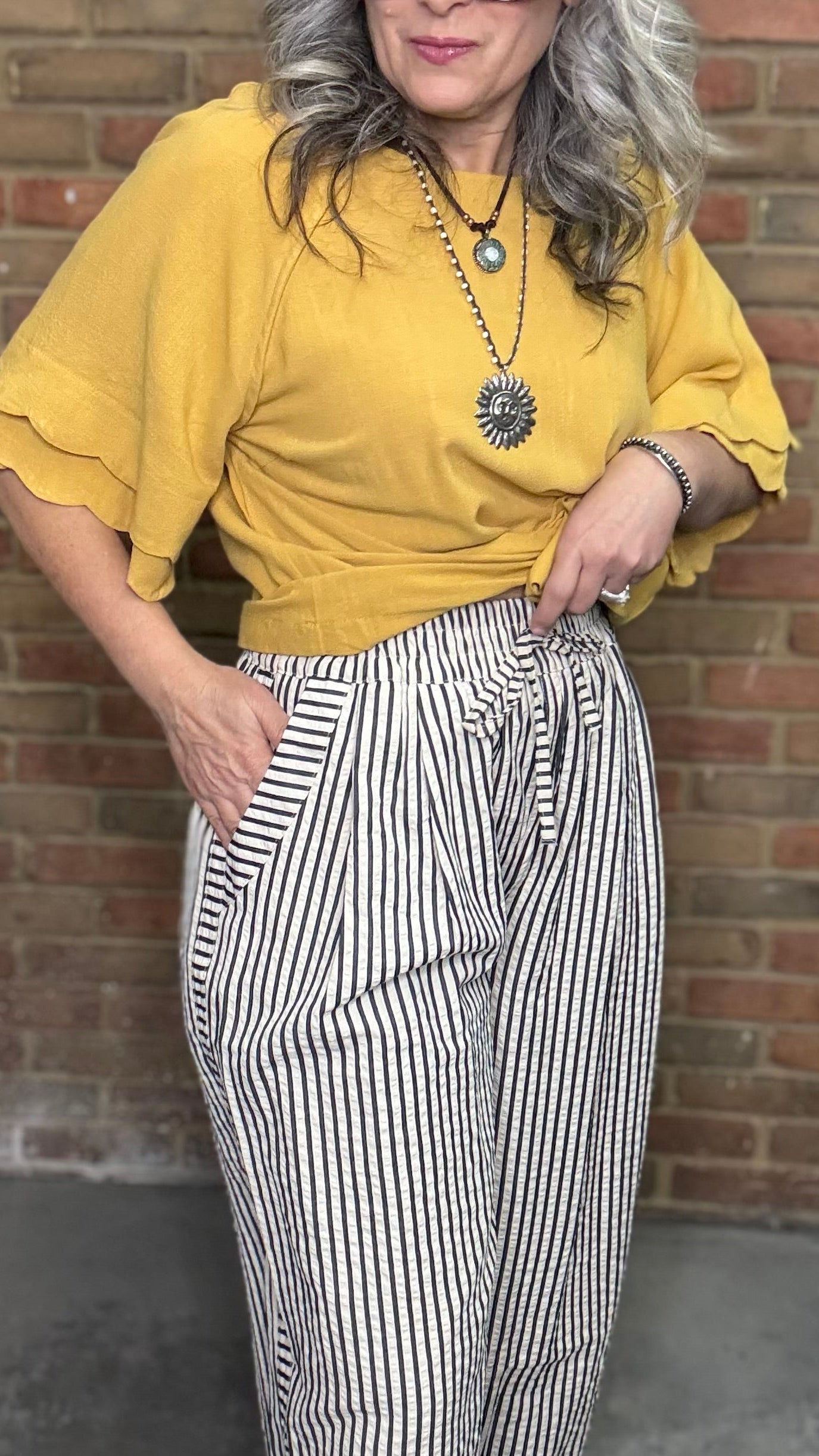 Woman in a mustard and Latte Wide Leg Pull On Pant standing against a brick wall.