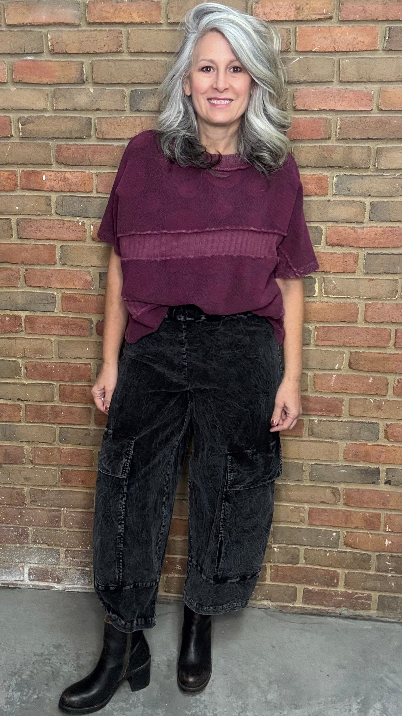 Person wearing a purple top and black pants standing against a brick wall.
