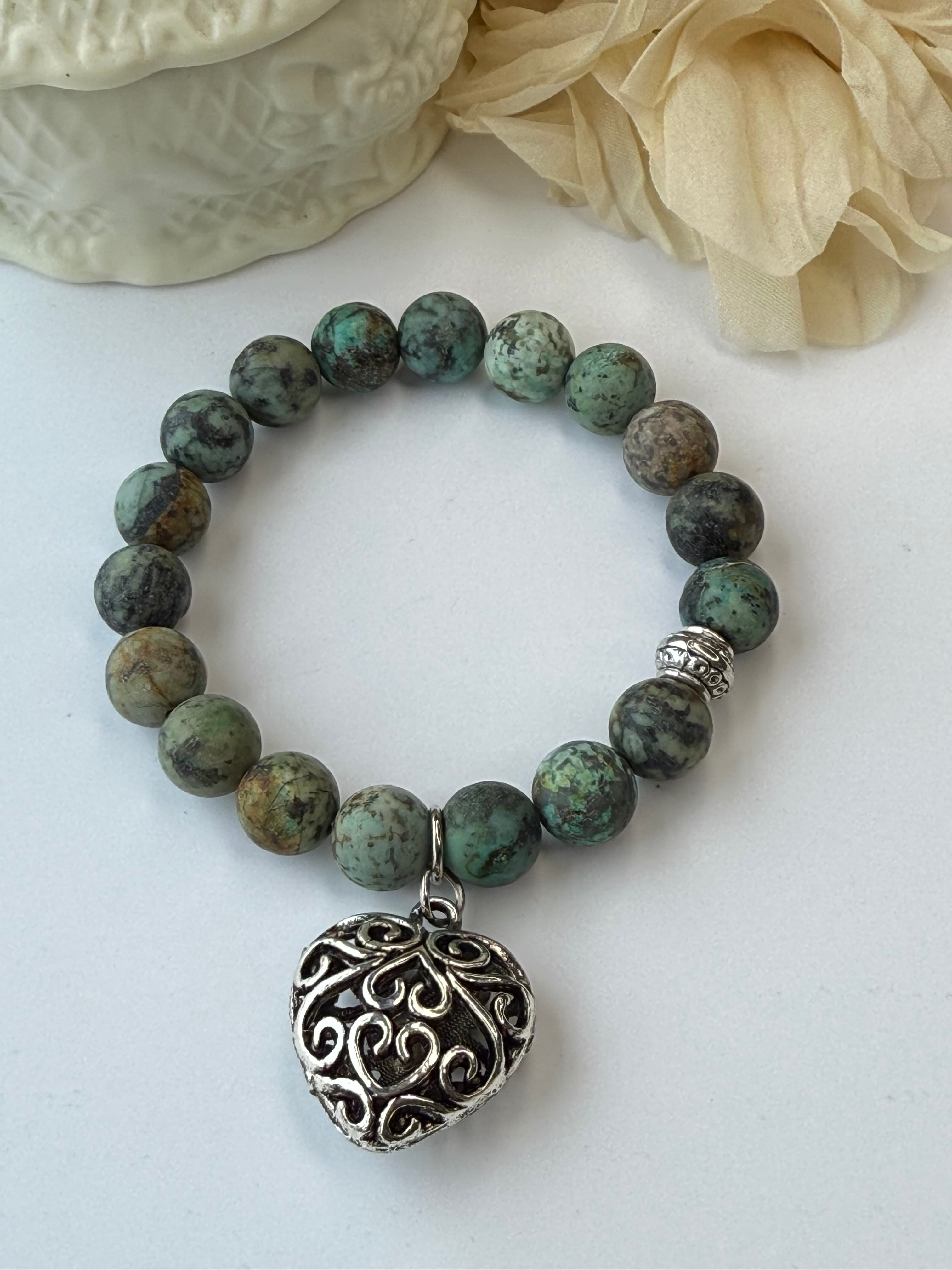 Green beaded bracelet with a silver heart-shaped charm on a white background
