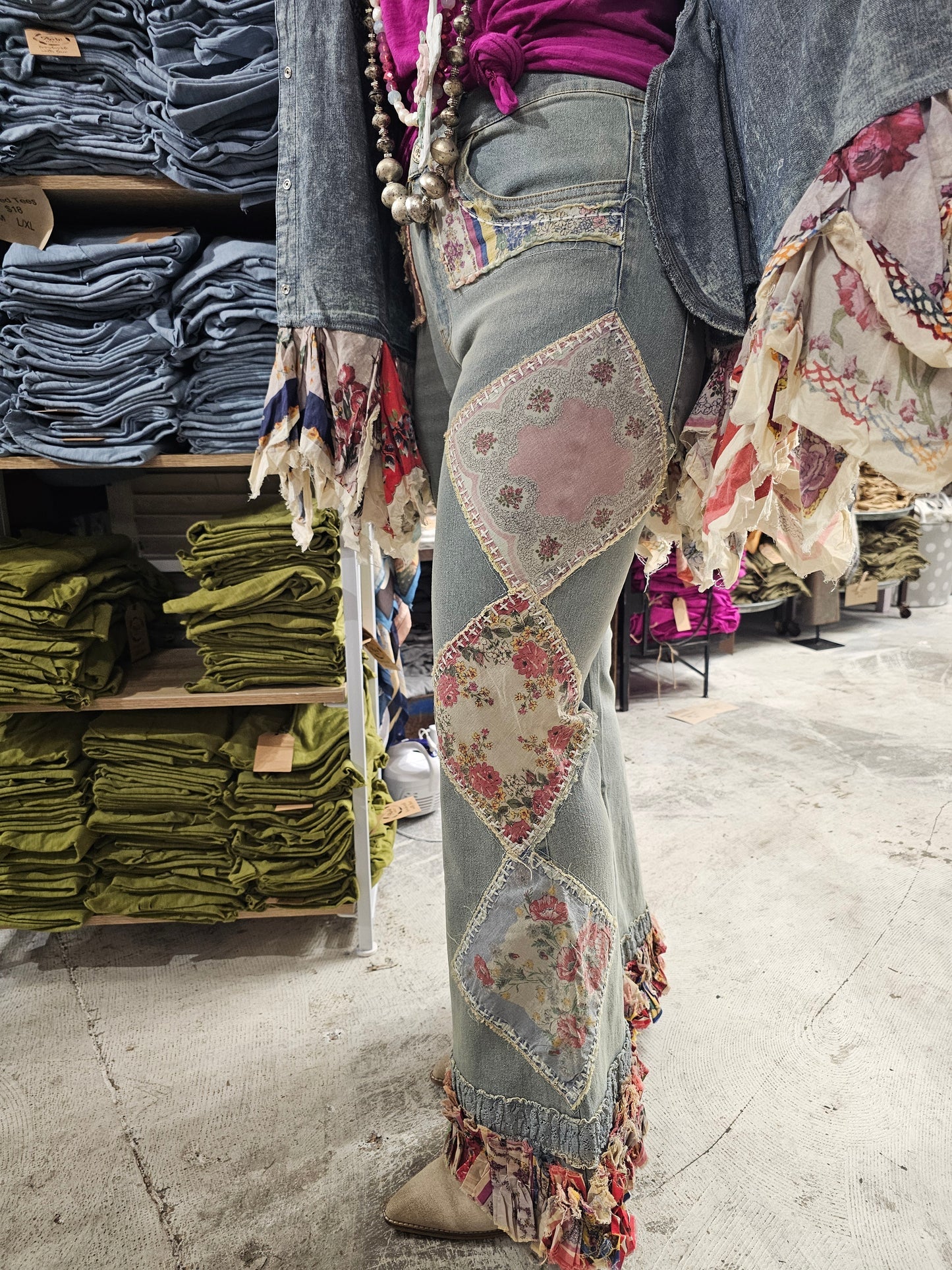 Person wearing a patterned pants in a store with stacks of clothes in the background.