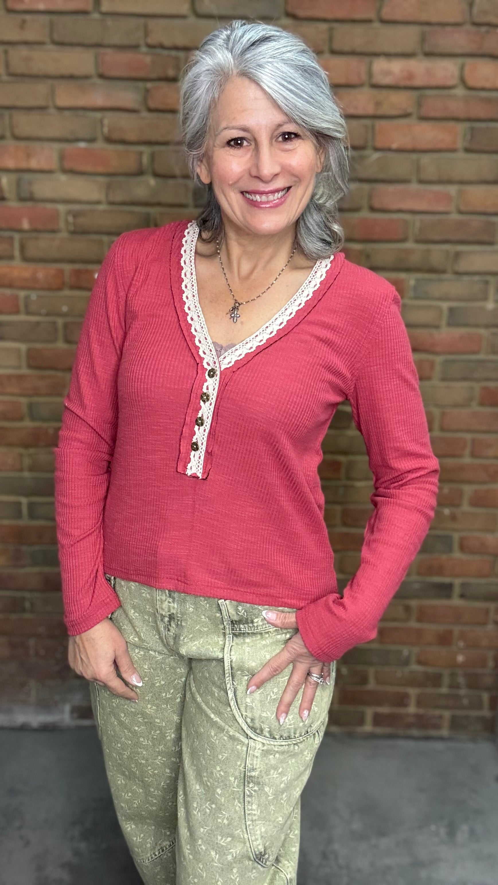 Woman wearing Raspberry Rose ribbed Henley Top with lace trim against a brick wall.