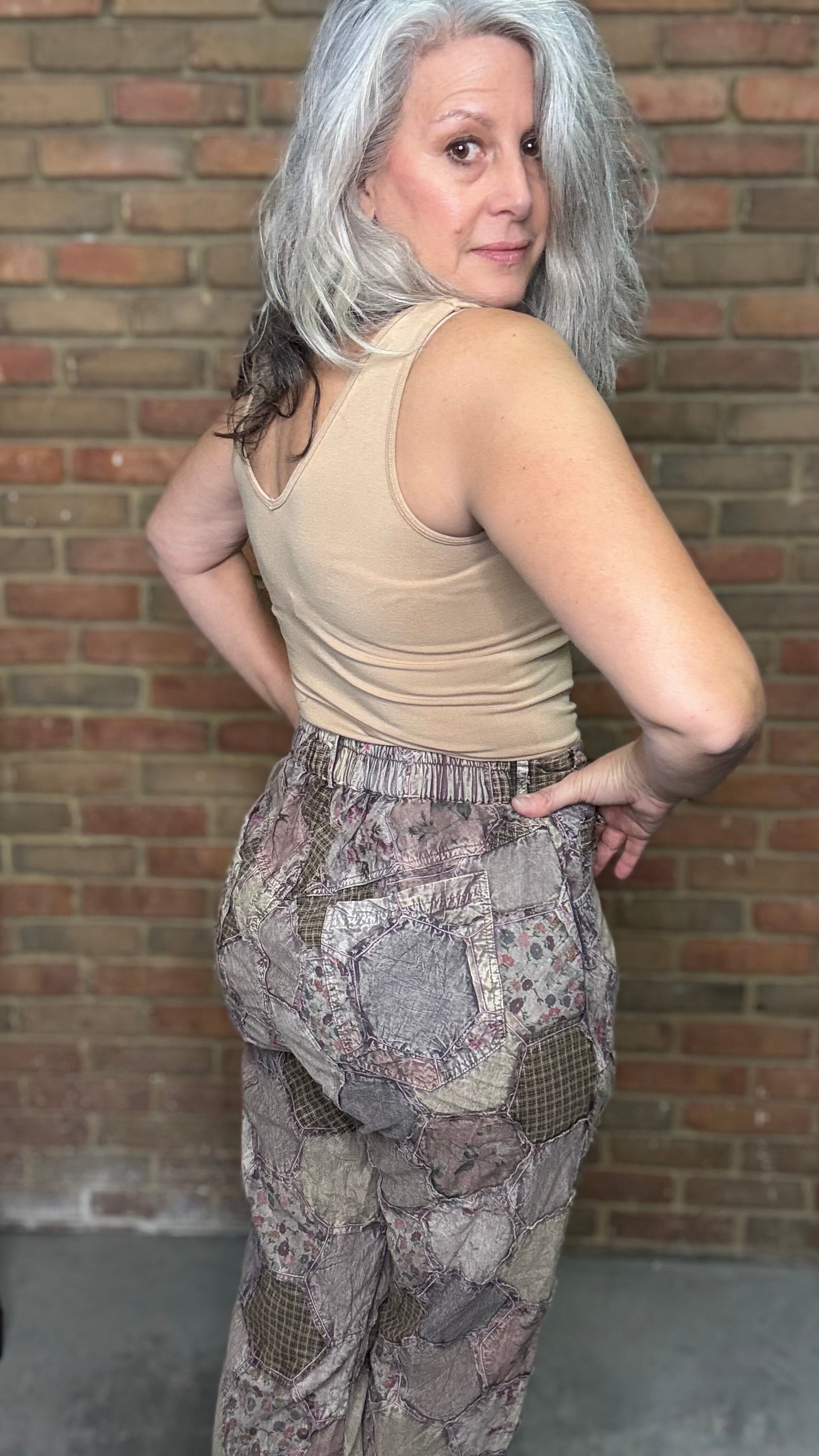 Person wearing a beige tank top and patterned pants against a brick wall.