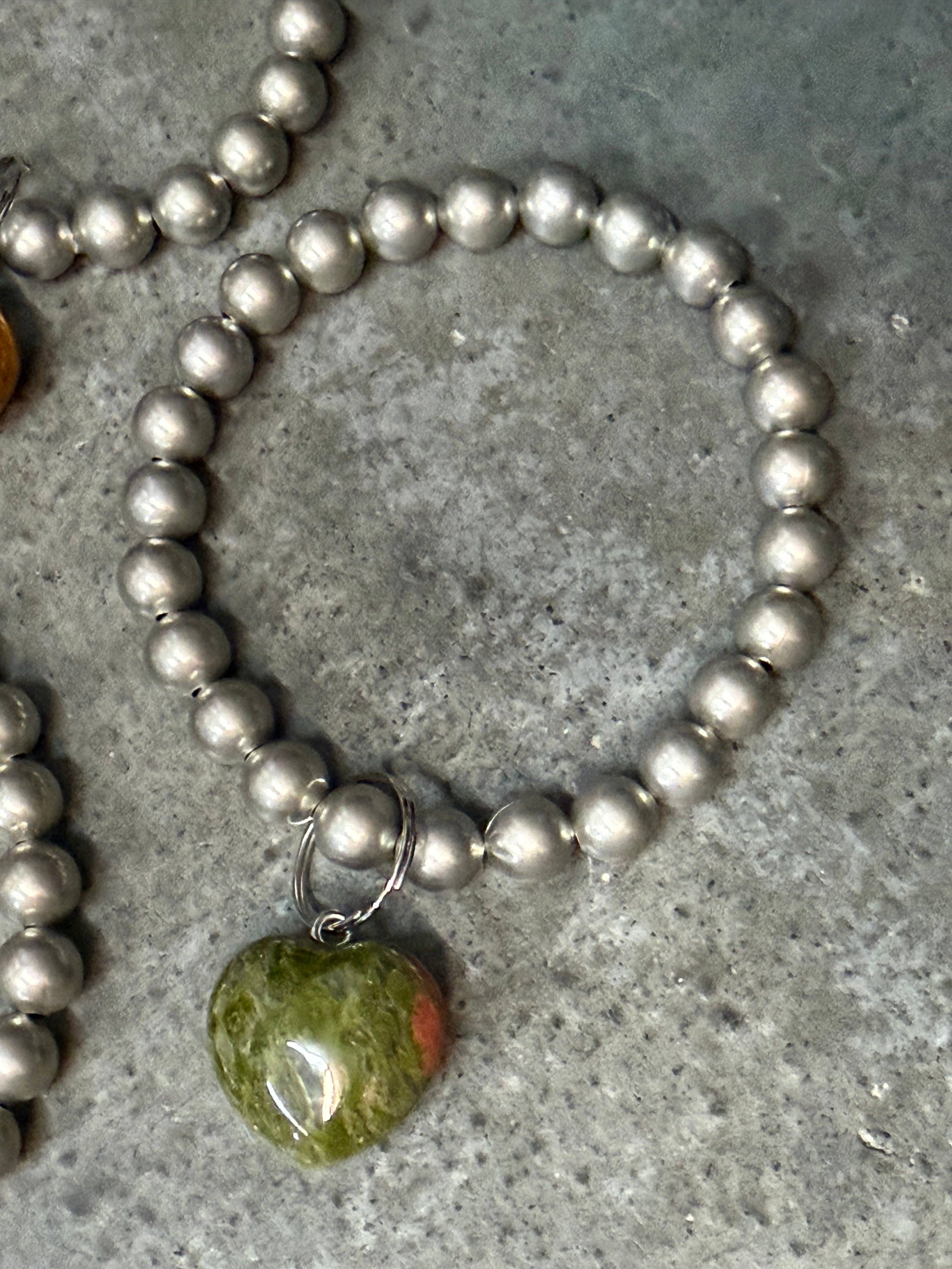 Silver beaded bracelet with a green stone pendant on a gray surface