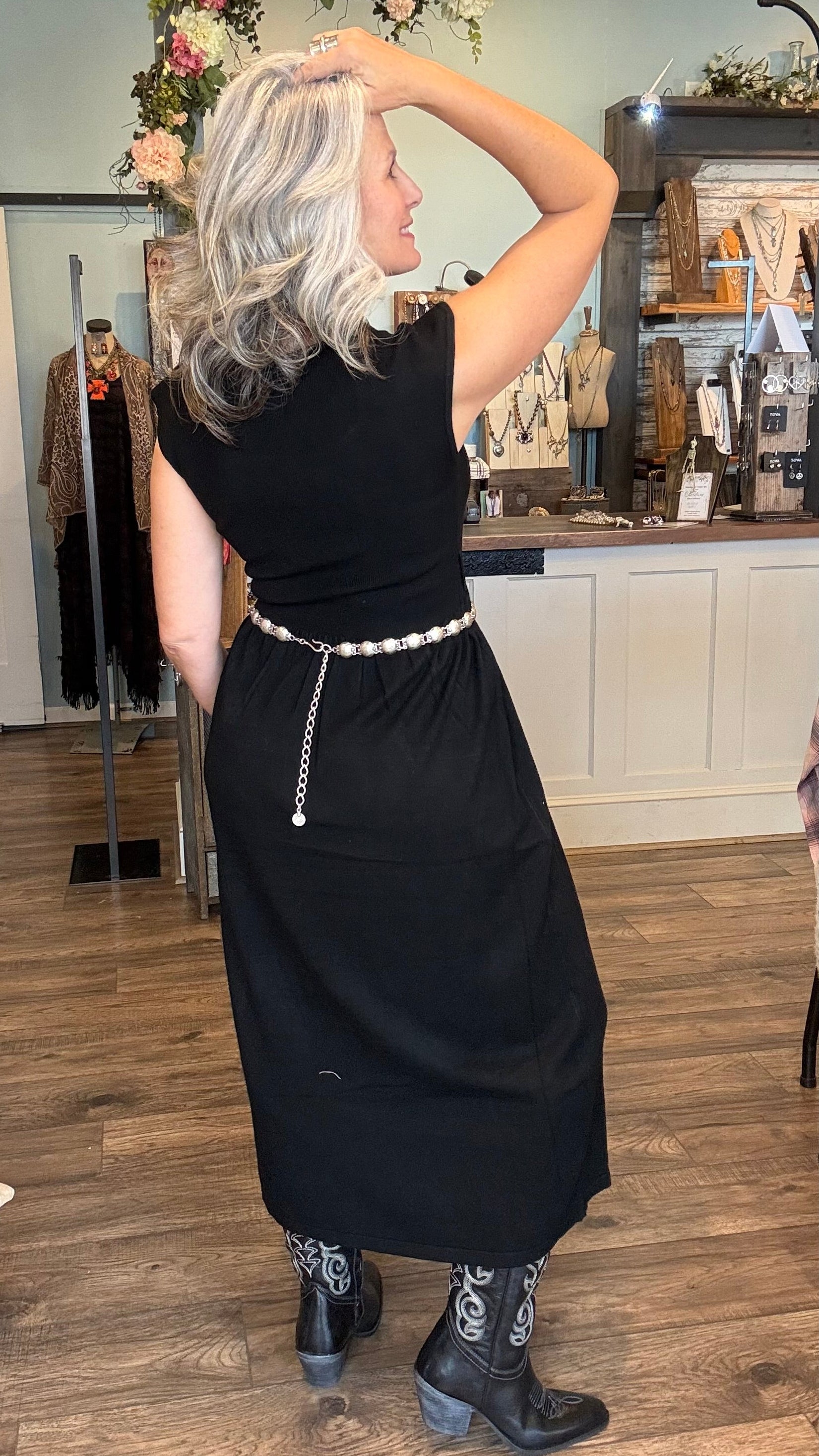 Woman in a black dress with a silver belt standing in a store.