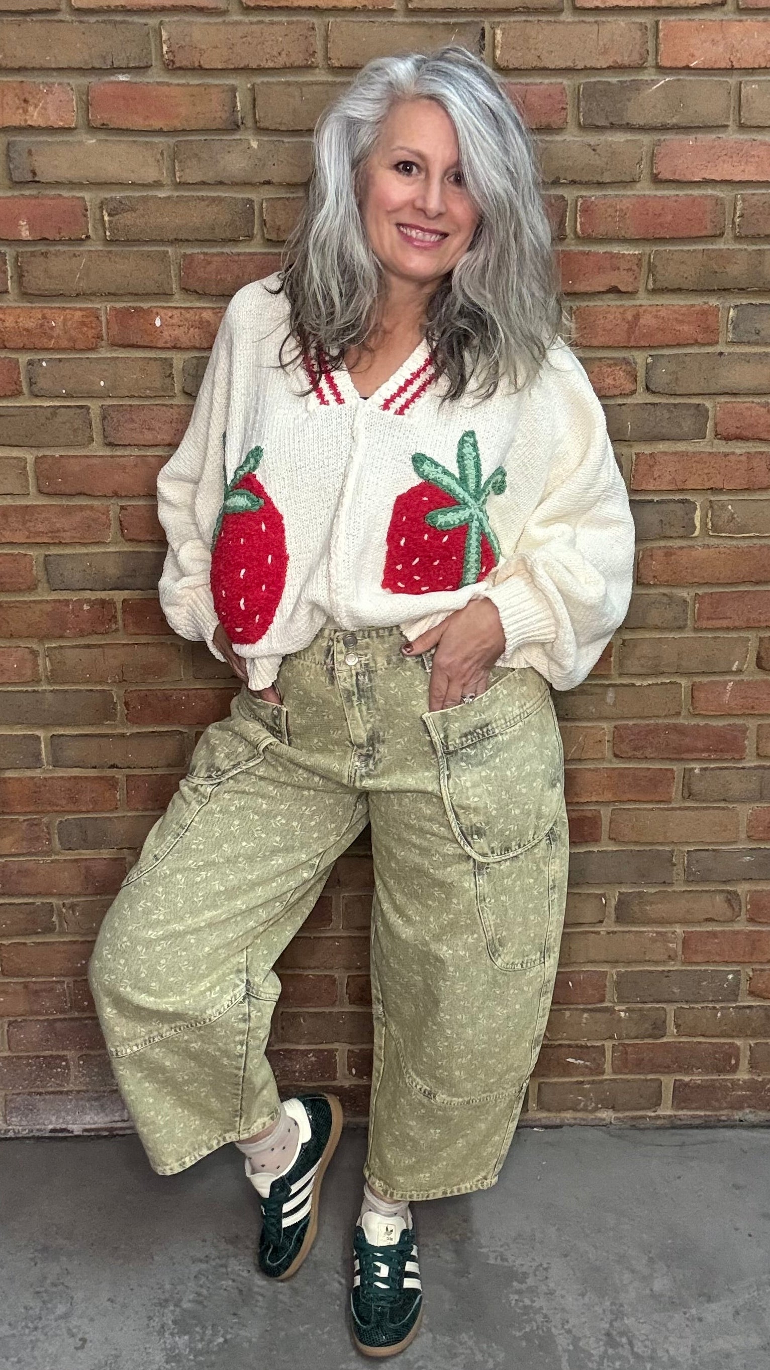 Person wearing the Strawberries on Cream Sweater and Floral Printed Barrel Pants standing against a brick wall.