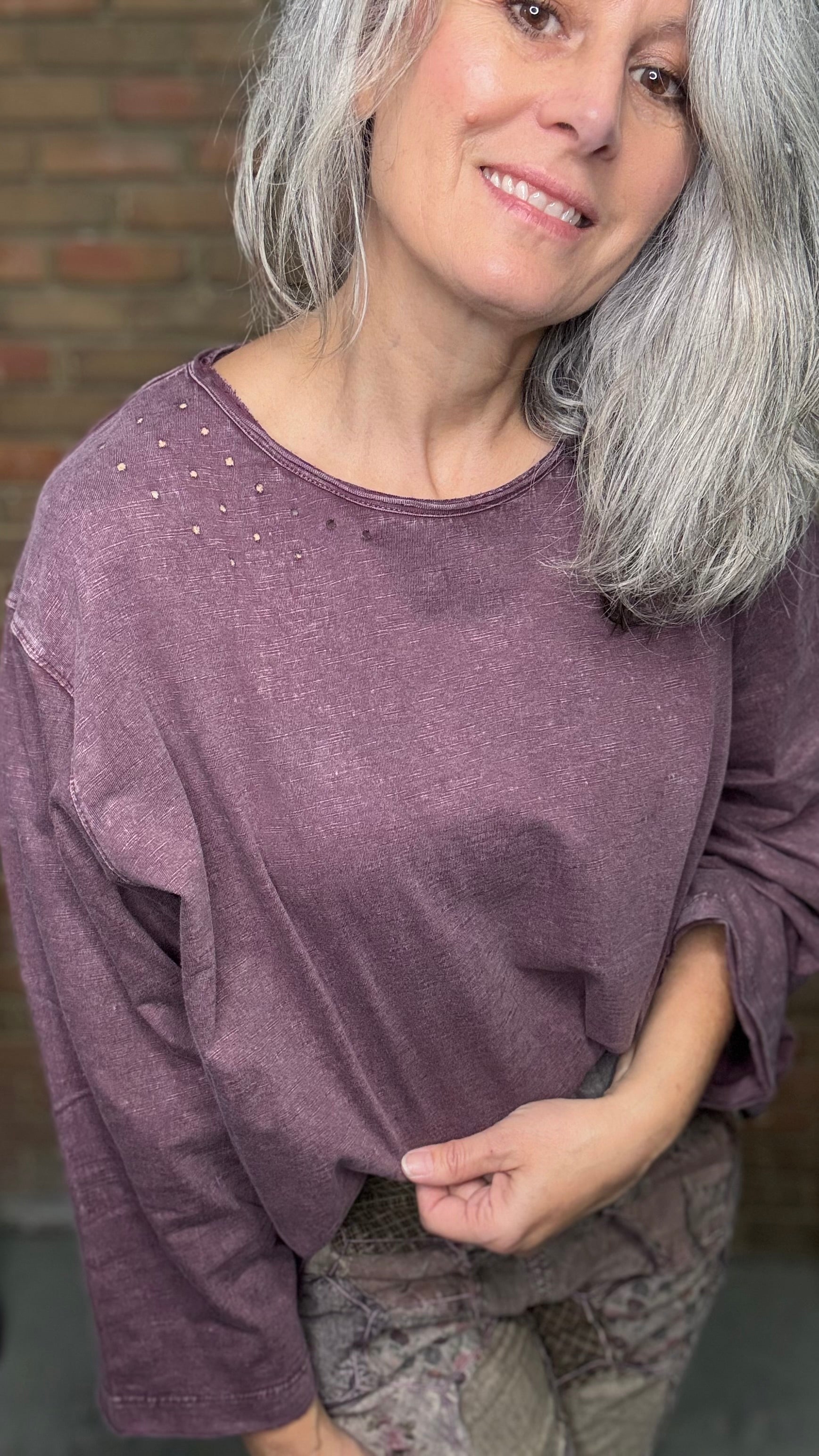 Woman wearing a purple long-sleeve top with a brick wall background