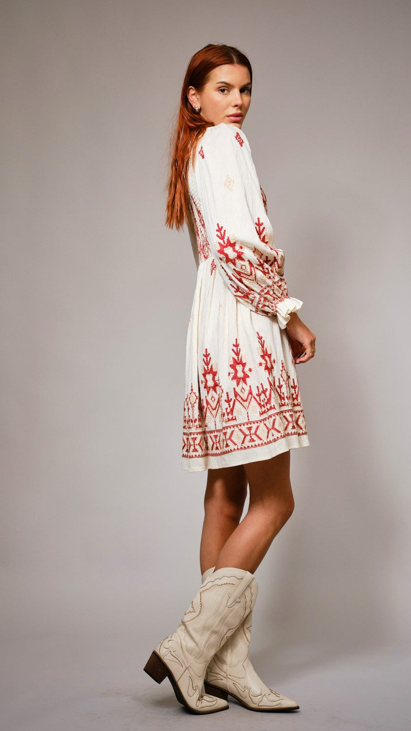 Woman wearing a white dress with red embroidery and white boots on a gray background