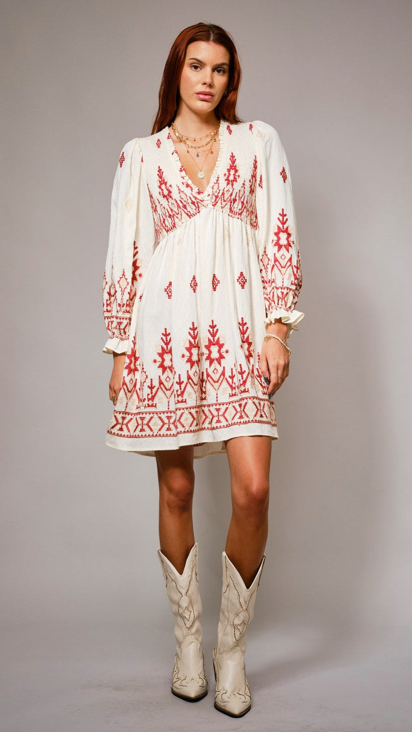 Woman wearing a white dress with red embroidery and white cowboy boots on a gray background