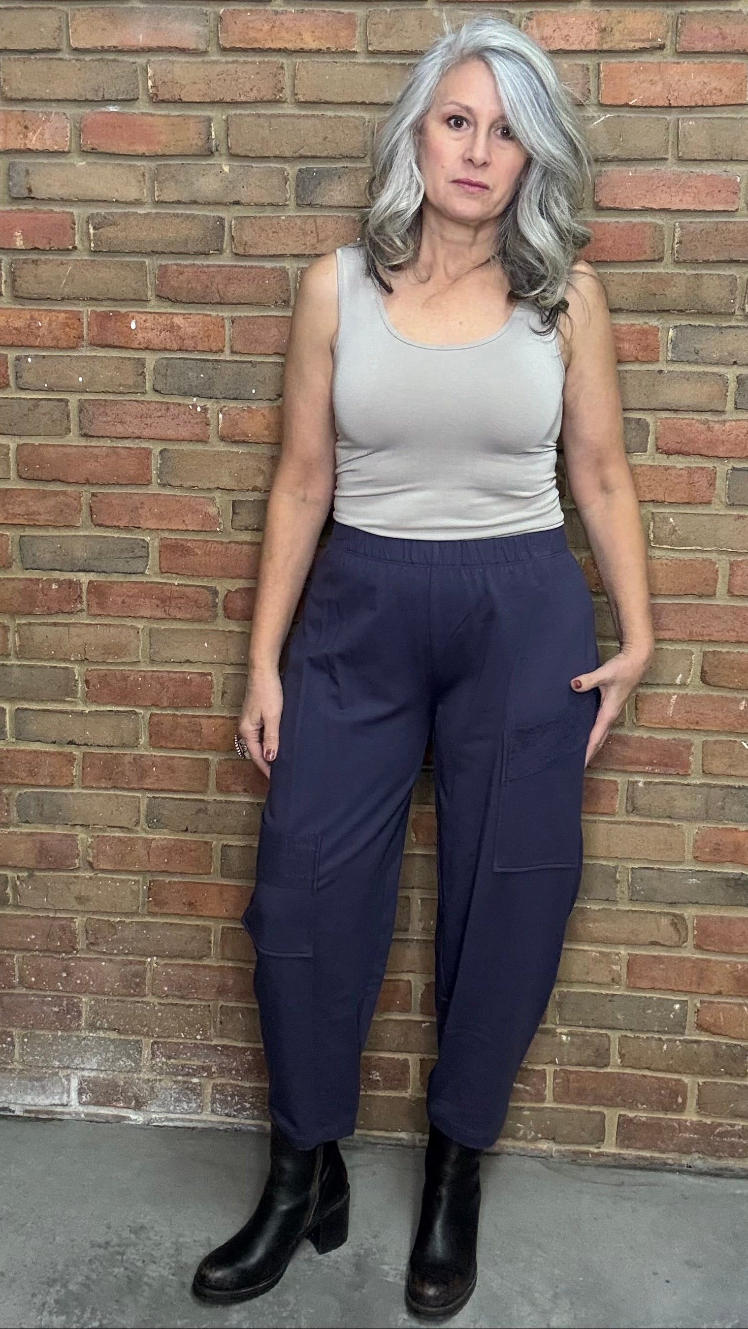 Woman standing against a brick wall wearing a tank top and the Mady Pant in plum.