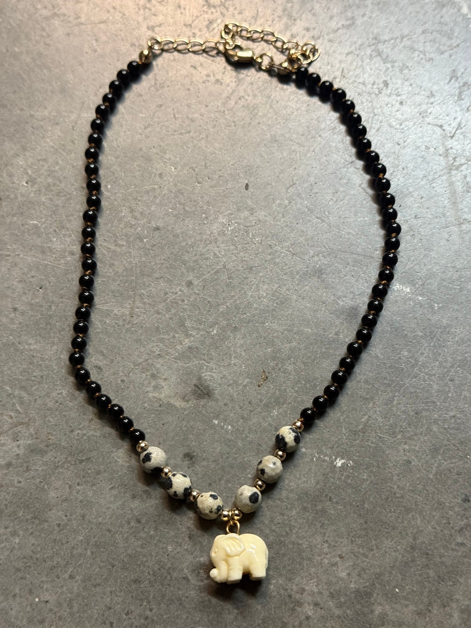 Necklace with black beads and a white elephant pendant on a gray surface