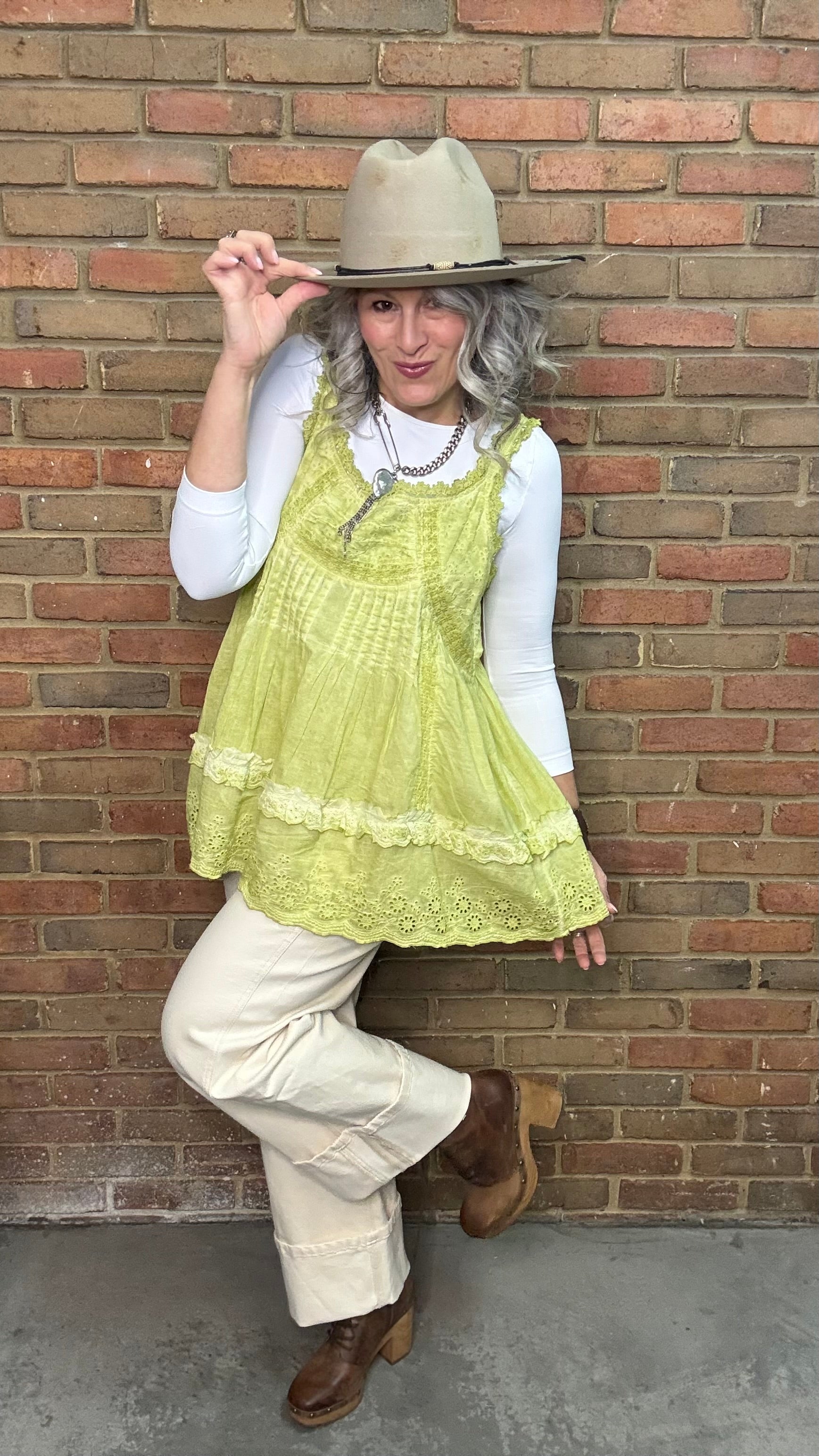 Woman wearing Eyelet Lace Tank over a white shirt, standing against a brick wall.