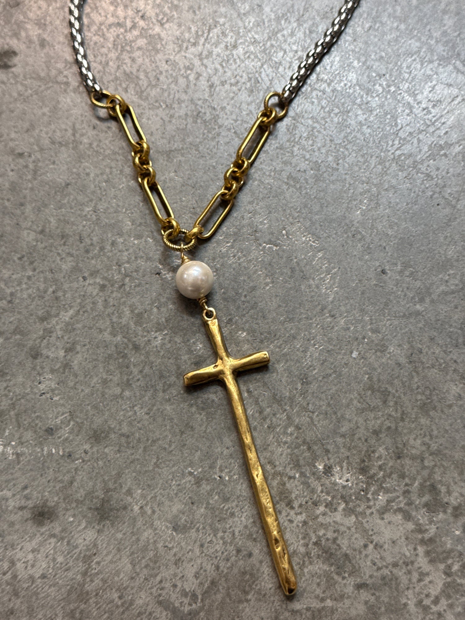 Necklace with a gold cross and pearl pendant on a gray surface