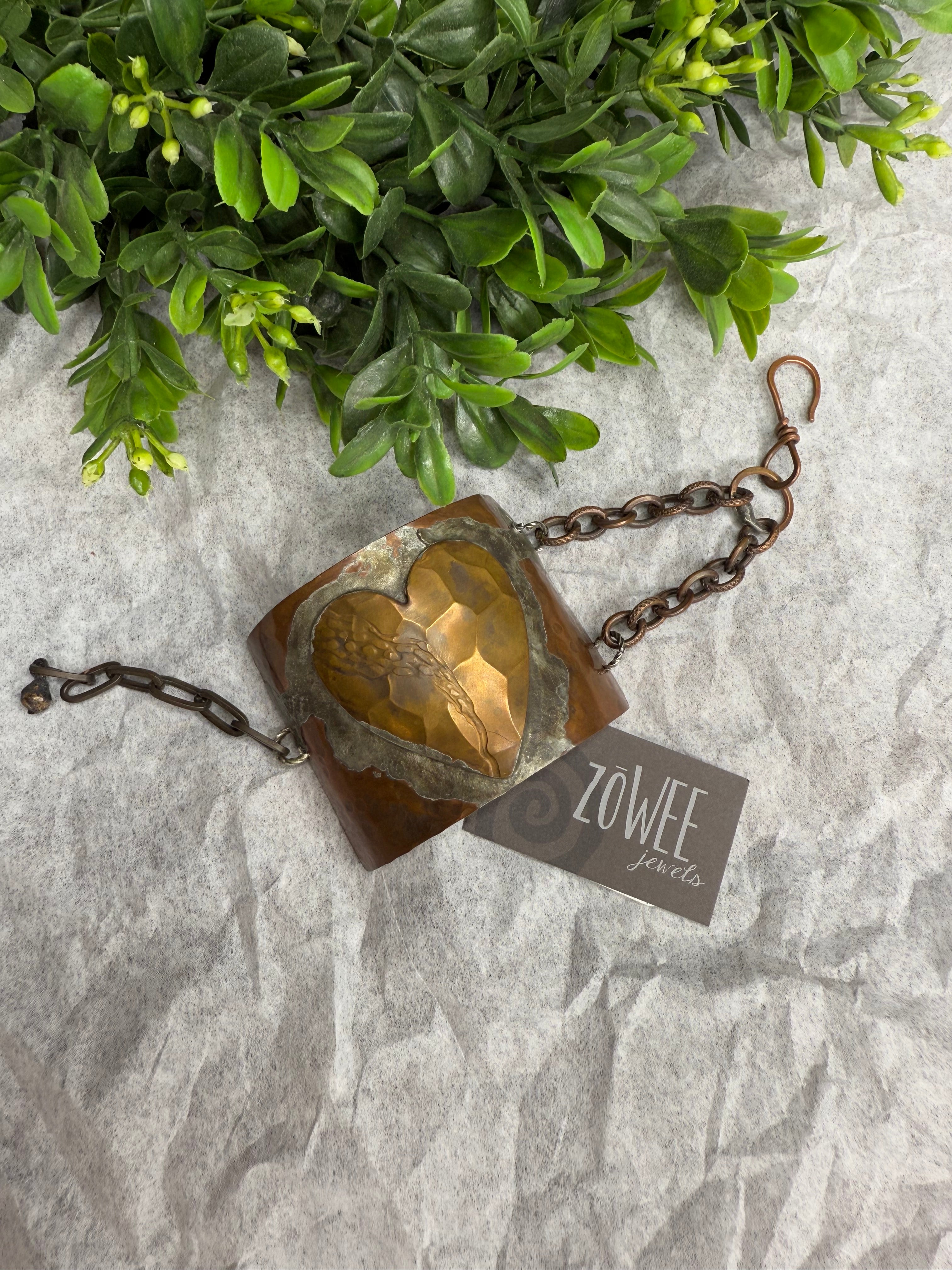 Half cuff with a soldered heart design on a textured surface with greenery