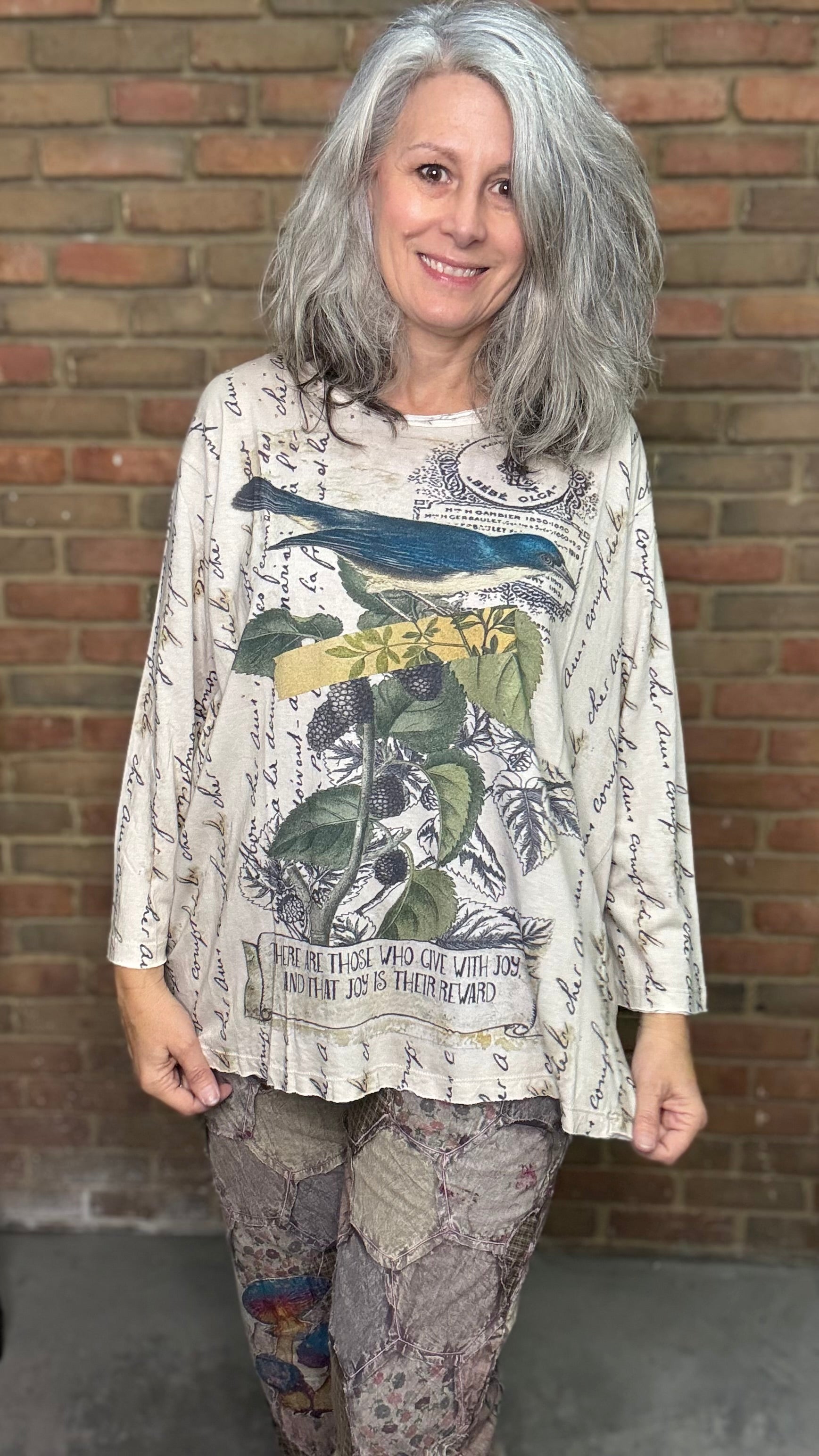 Woman wearing a patterned shirt with a bird design in front of a brick wall.