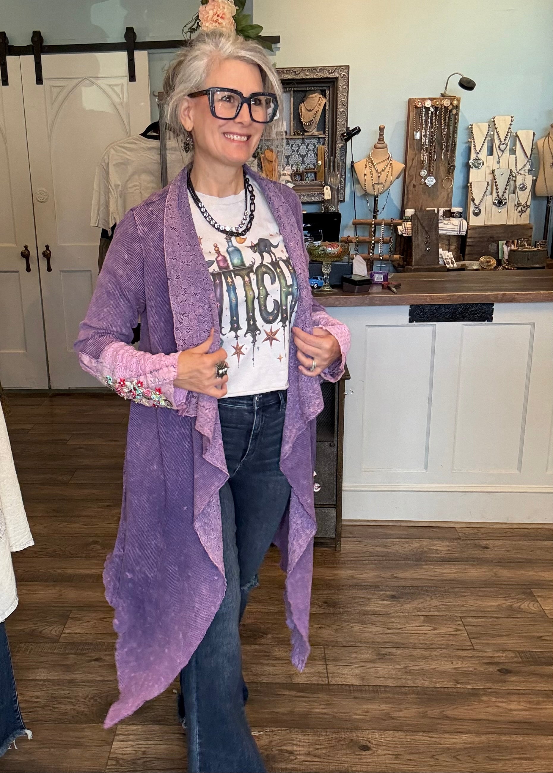 Woman wearing a purple cardigan over a graphic t-shirt in a jewelry store.