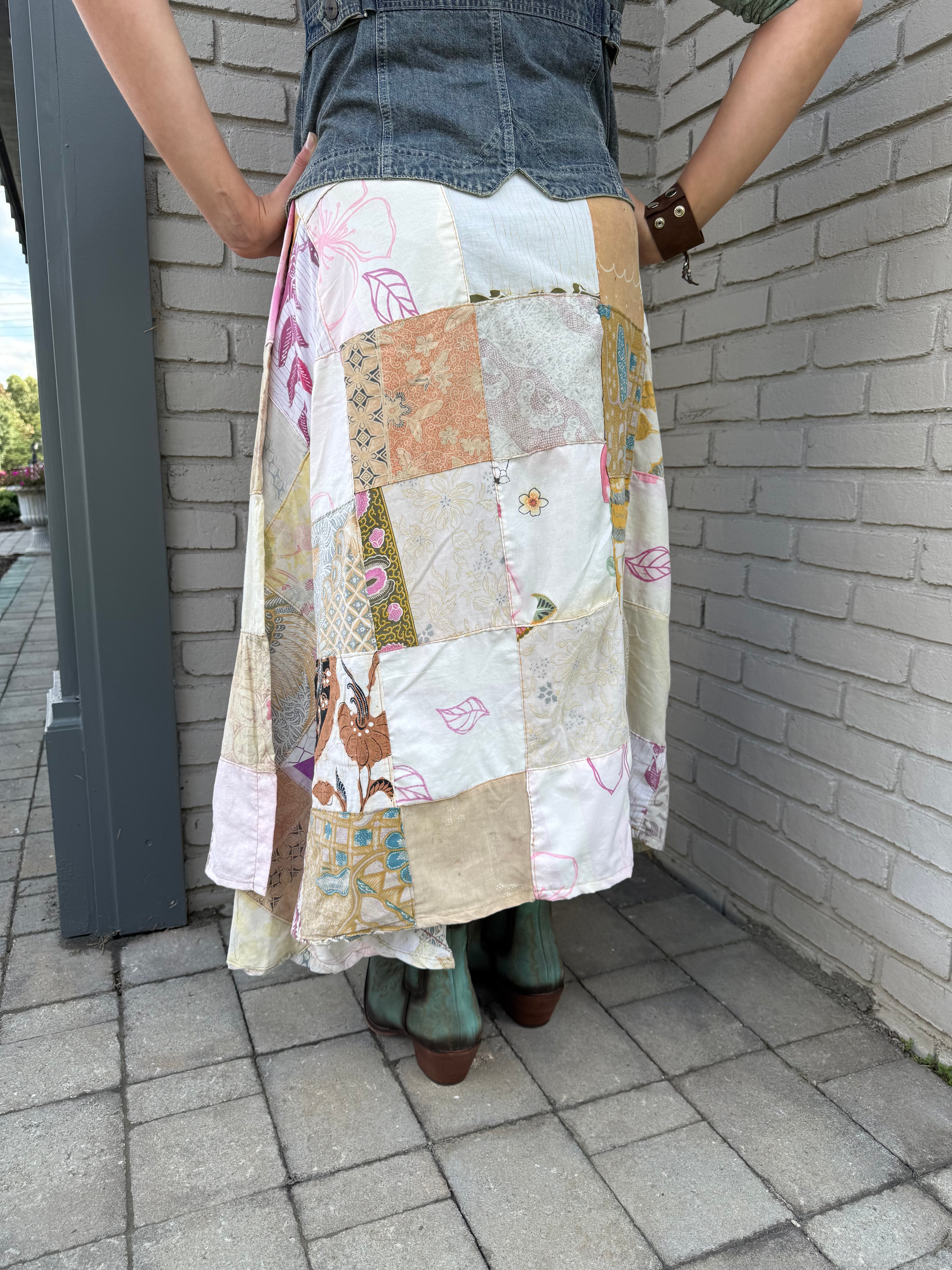 Back of a woman wearing a patchwork skirt standing at the corner of a building.