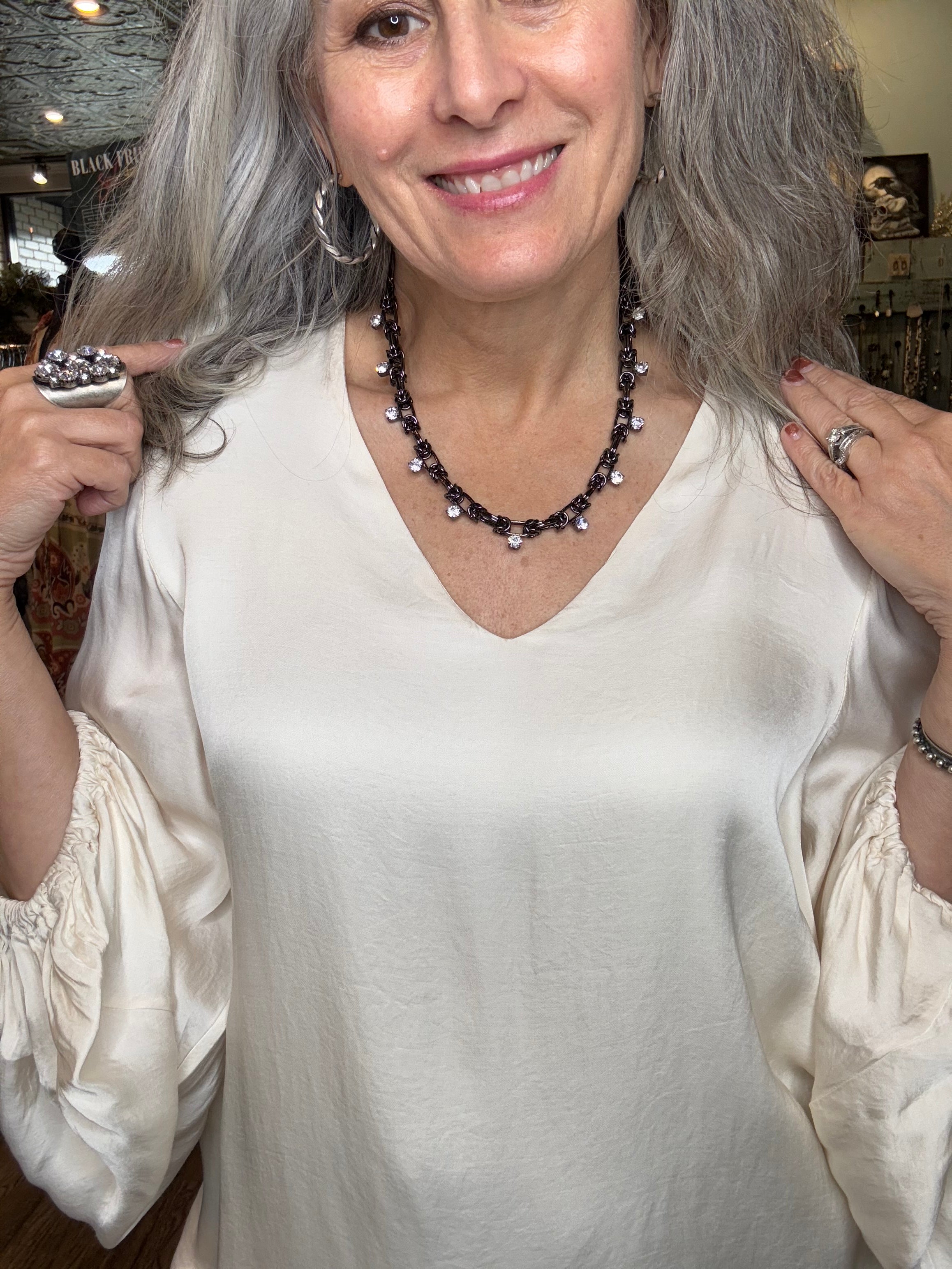 Woman with gray hair wearing a white dress and black beaded necklace, smiling.