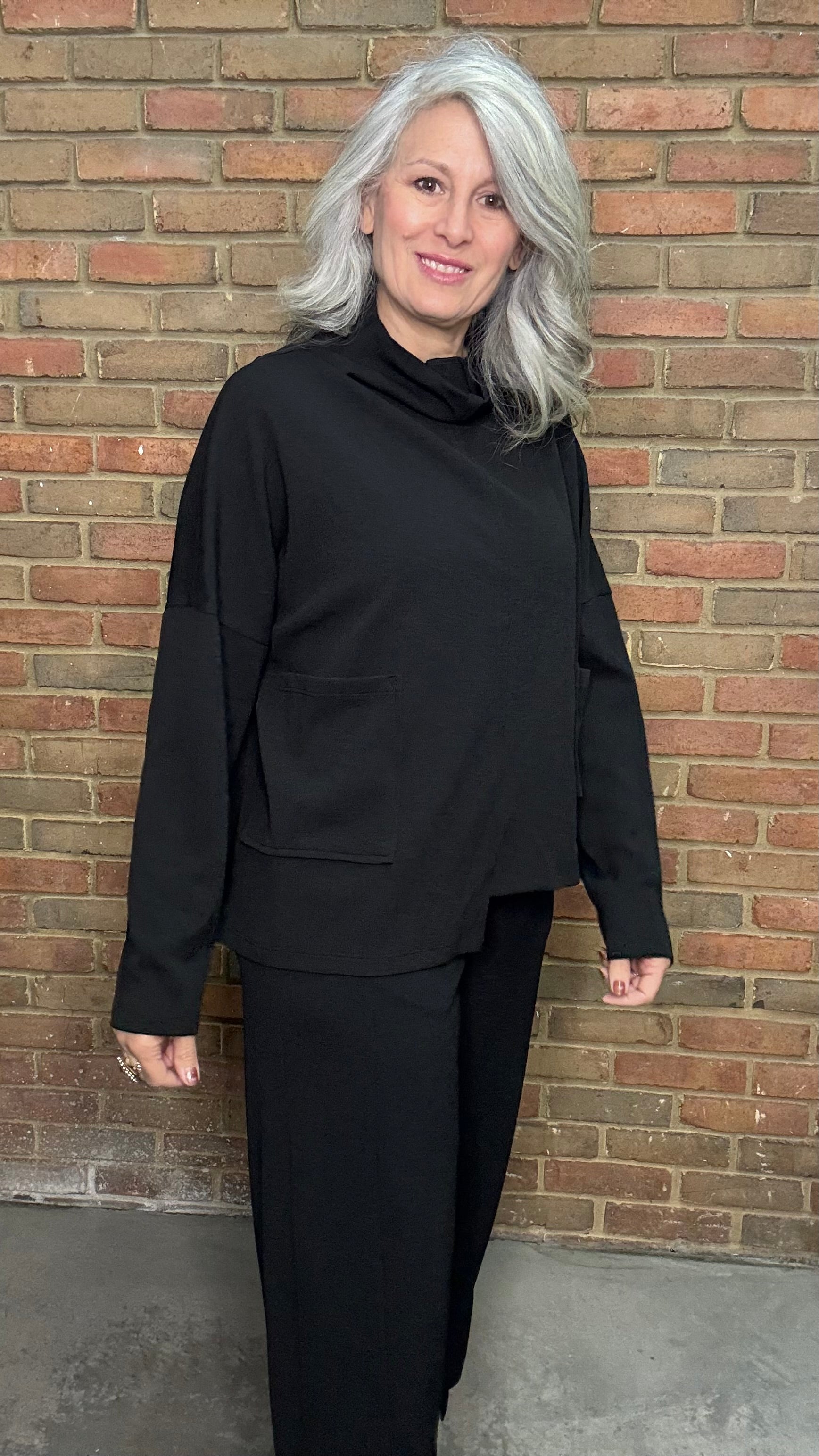 Person wearing a black outfit standing against a brick wall