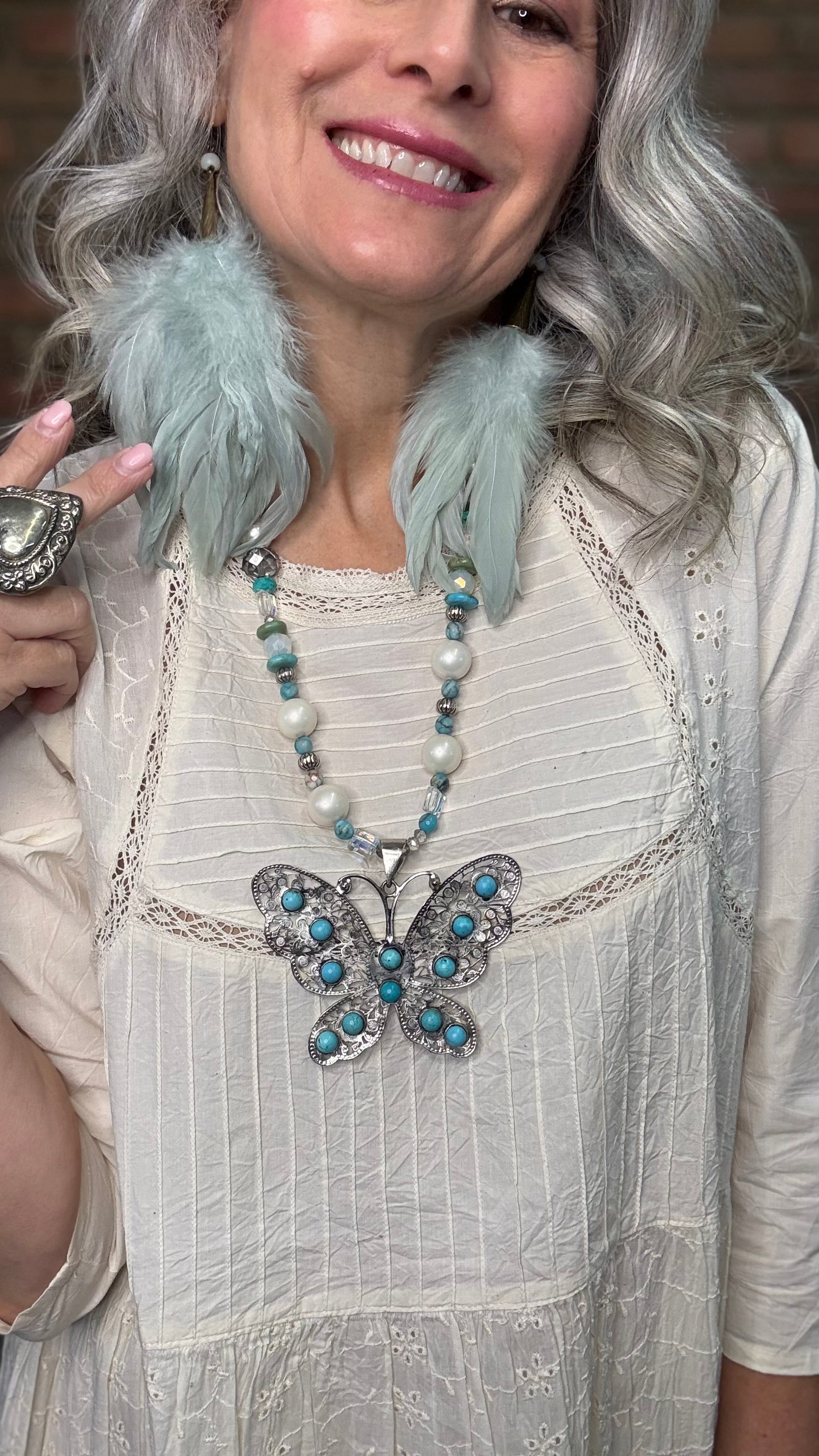 Woman wearing Silver Filigree Butterfly Necklace with turquoise stones and sage feather earrings.