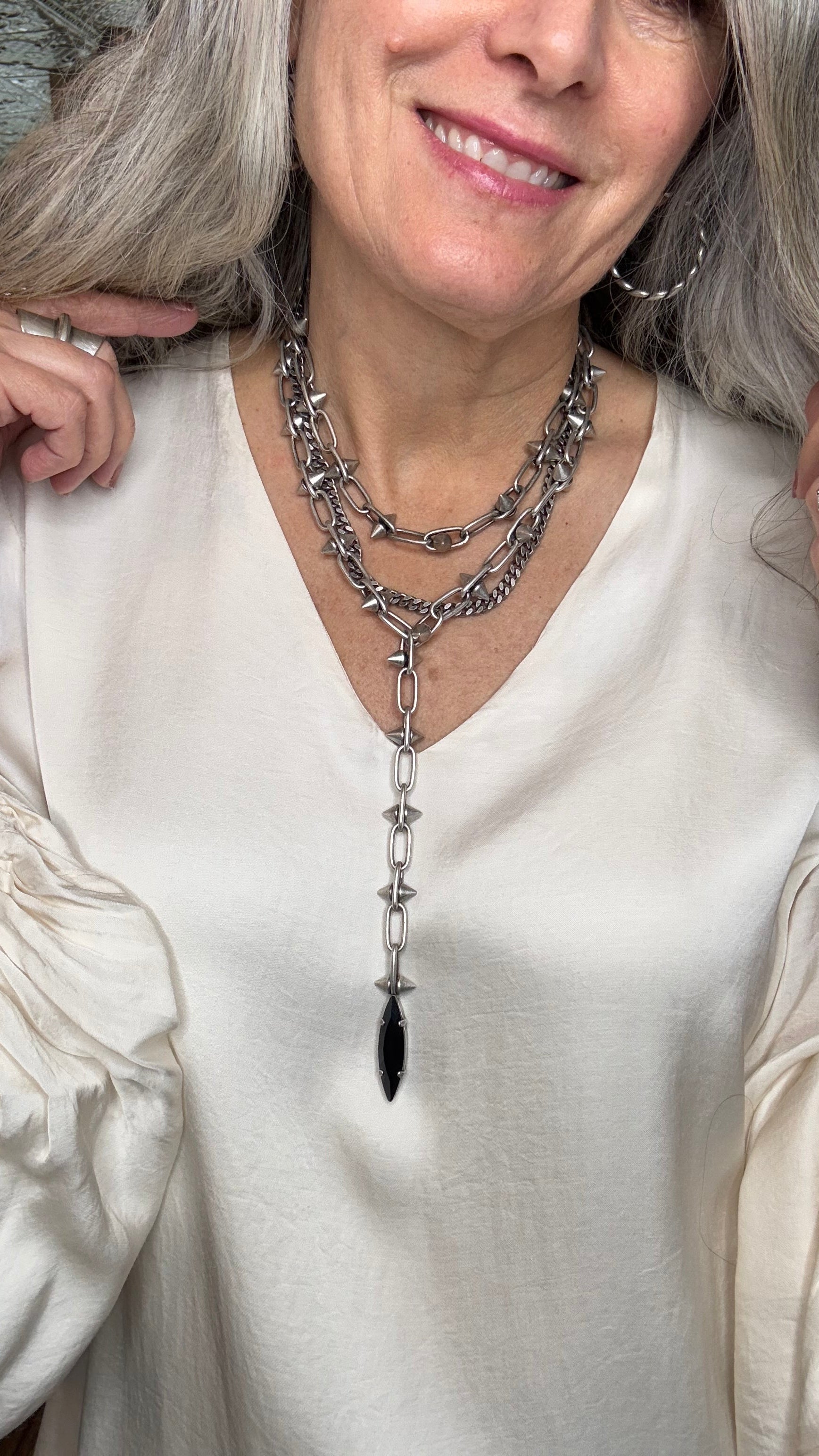 Woman wearing a silver necklace with a black accent, lying on a white surface.