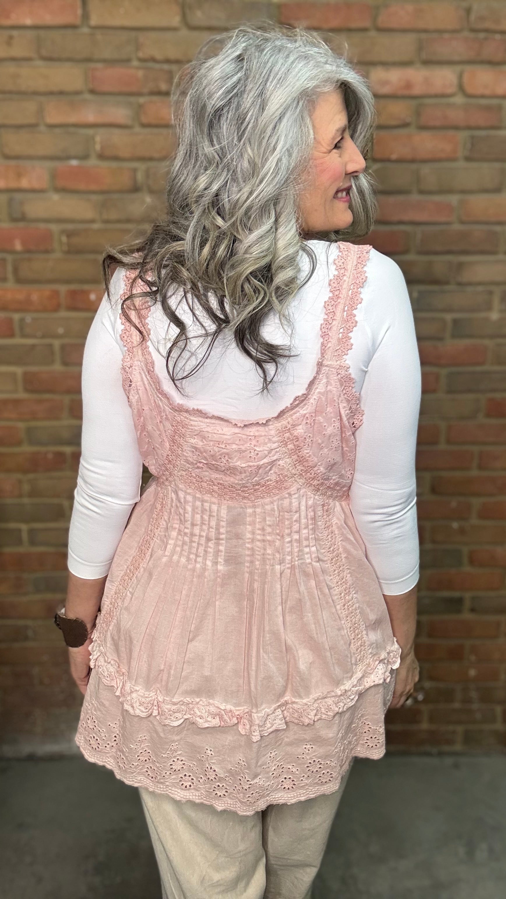 Woman wearing Eyelet Lace Tank over a white shirt, standing against a brick wall.