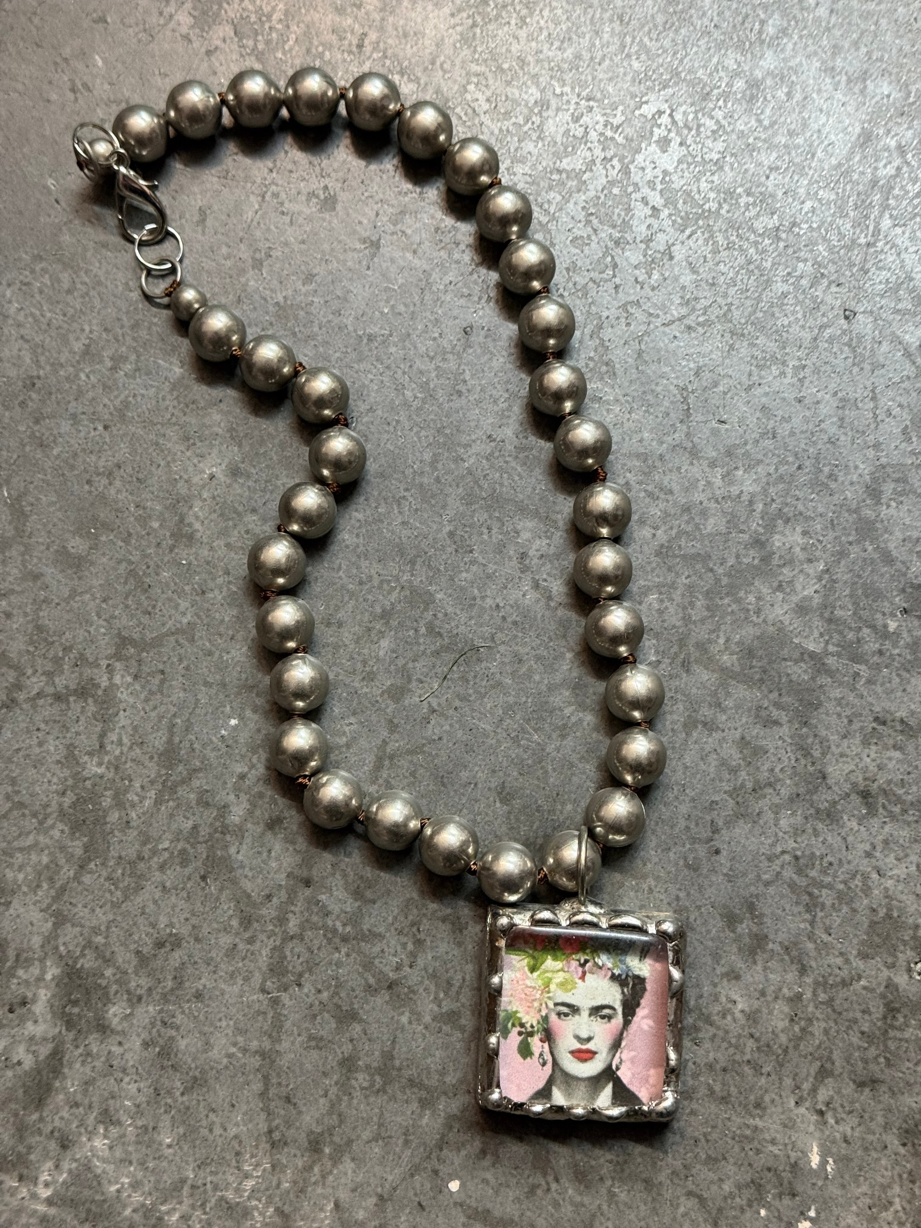 Necklace with beaded design and a square charm on a gray surface