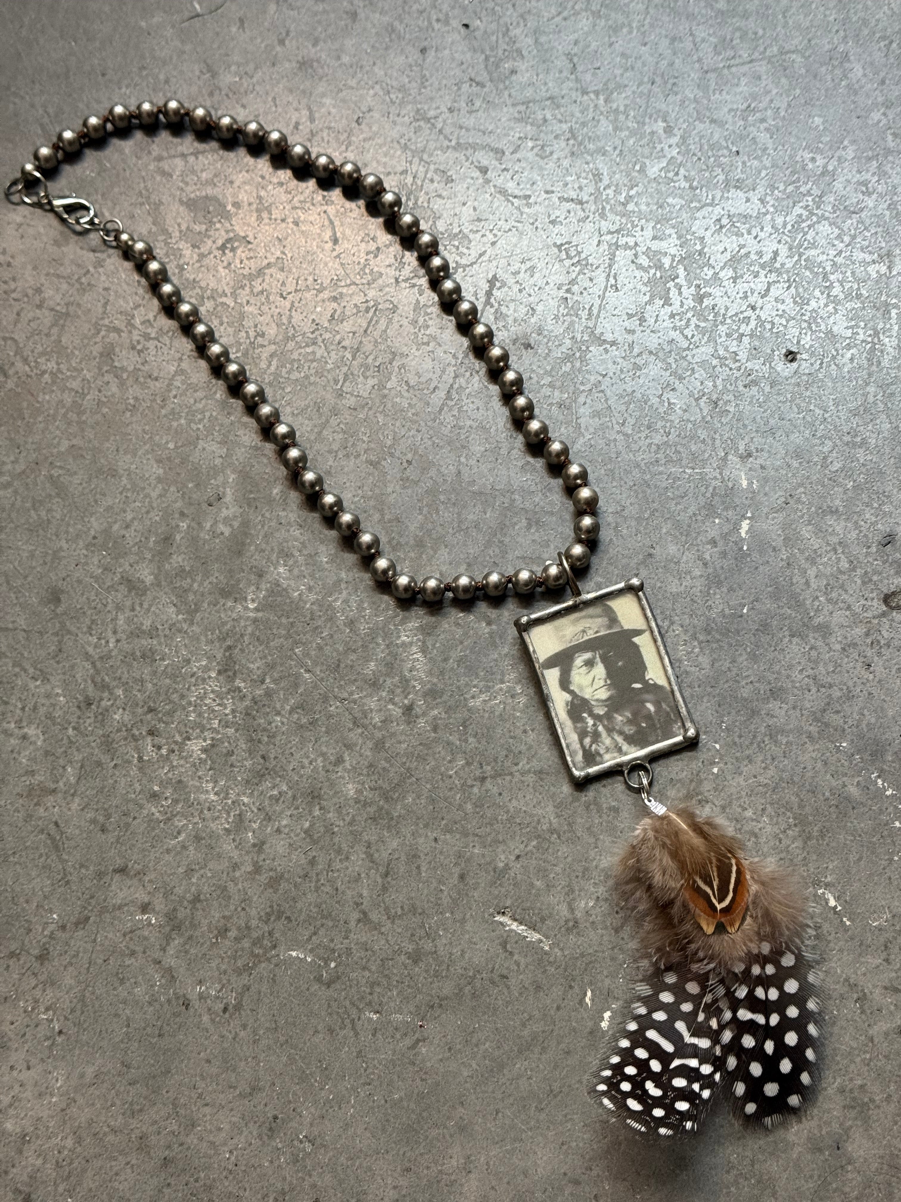 Necklace with feather charm and photo pendant on a textured surface