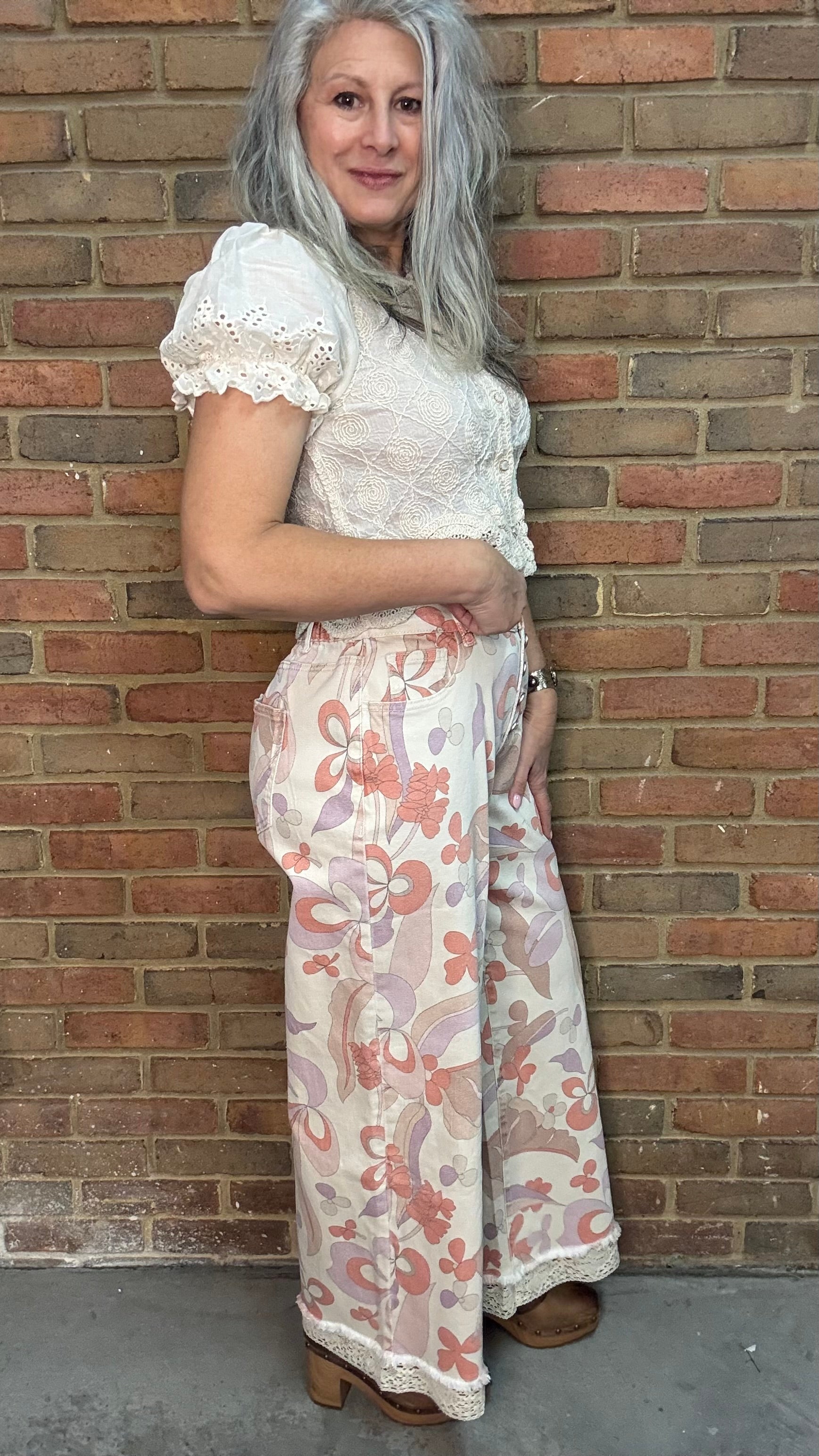 Woman wearing the Groovy Print Denim Pants standing against a brick wall.