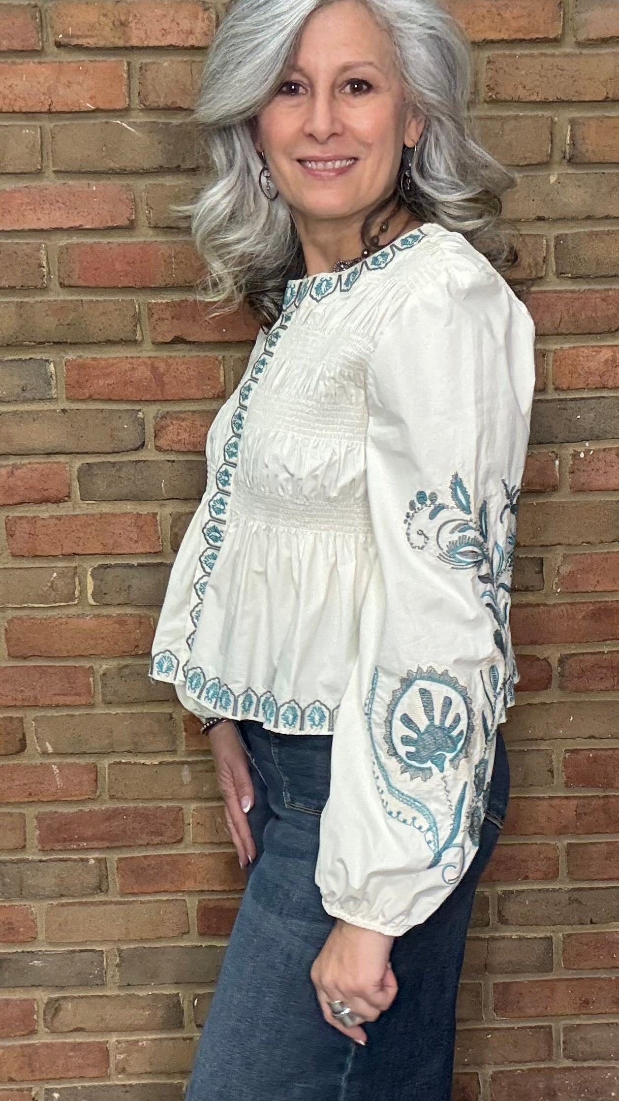 Woman wearing the Embroideried Smocked Peasant Top and Judy Blue Palazzo jeans against a brick wall.