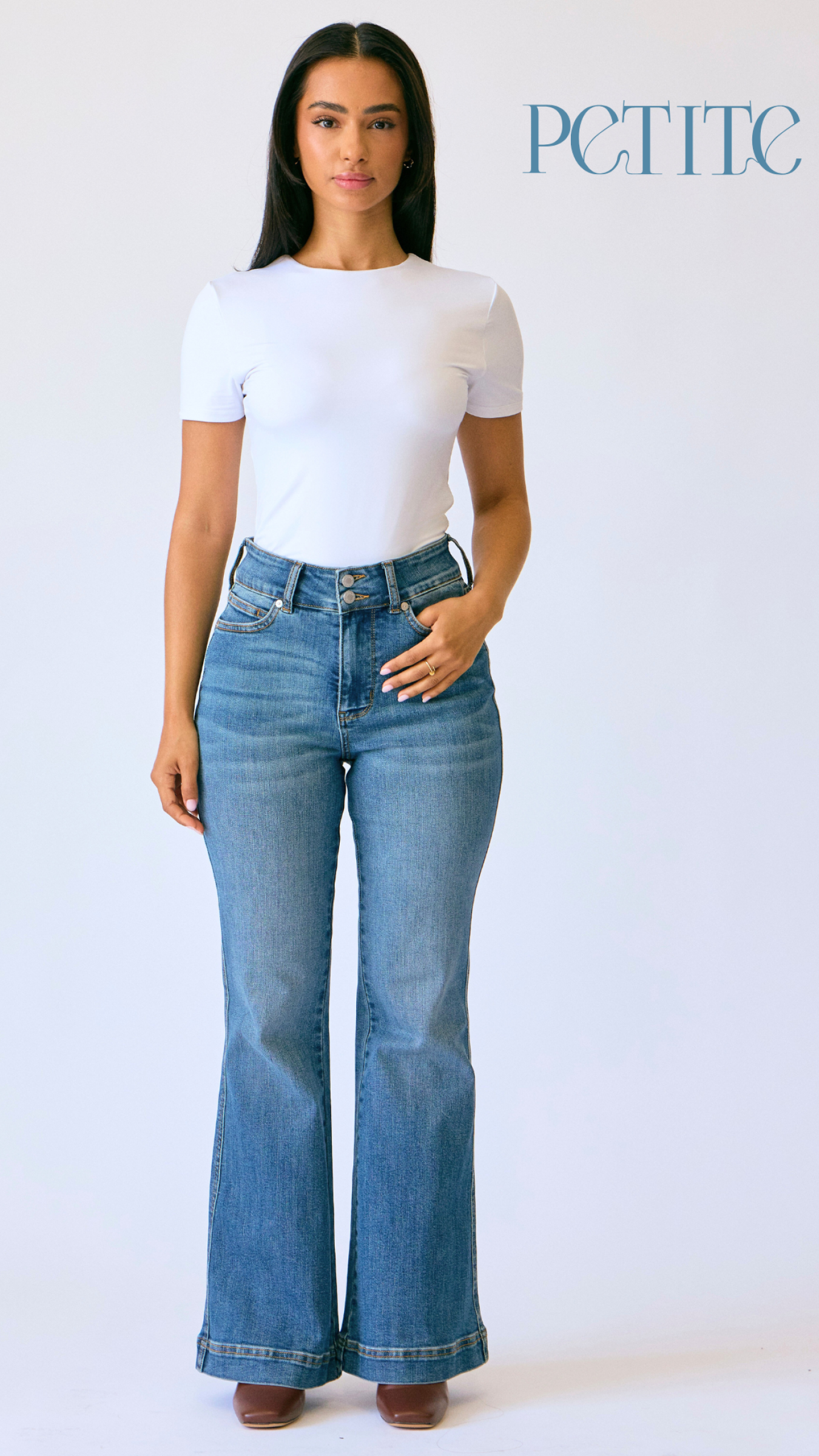 Woman wearing a white t-shirt and blue flared jeans on a plain background