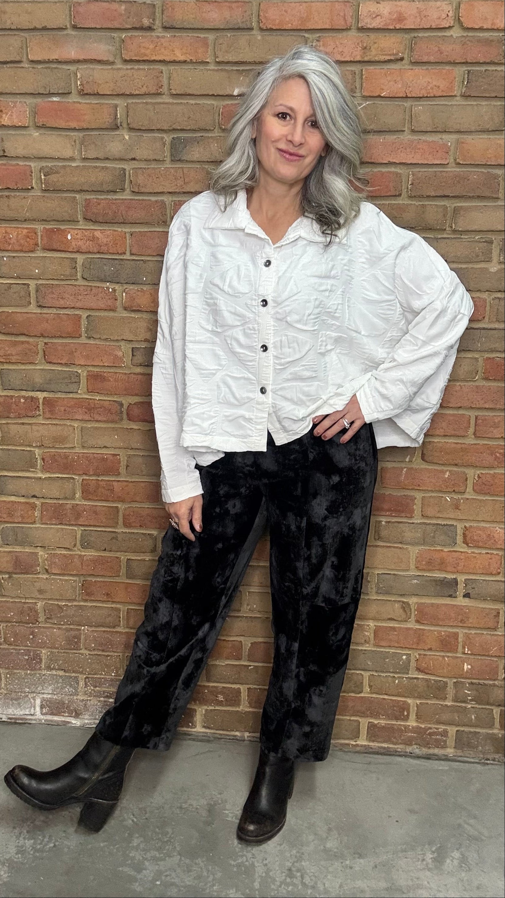 Woman in a white shirt and black pants leaning against a brick wall.