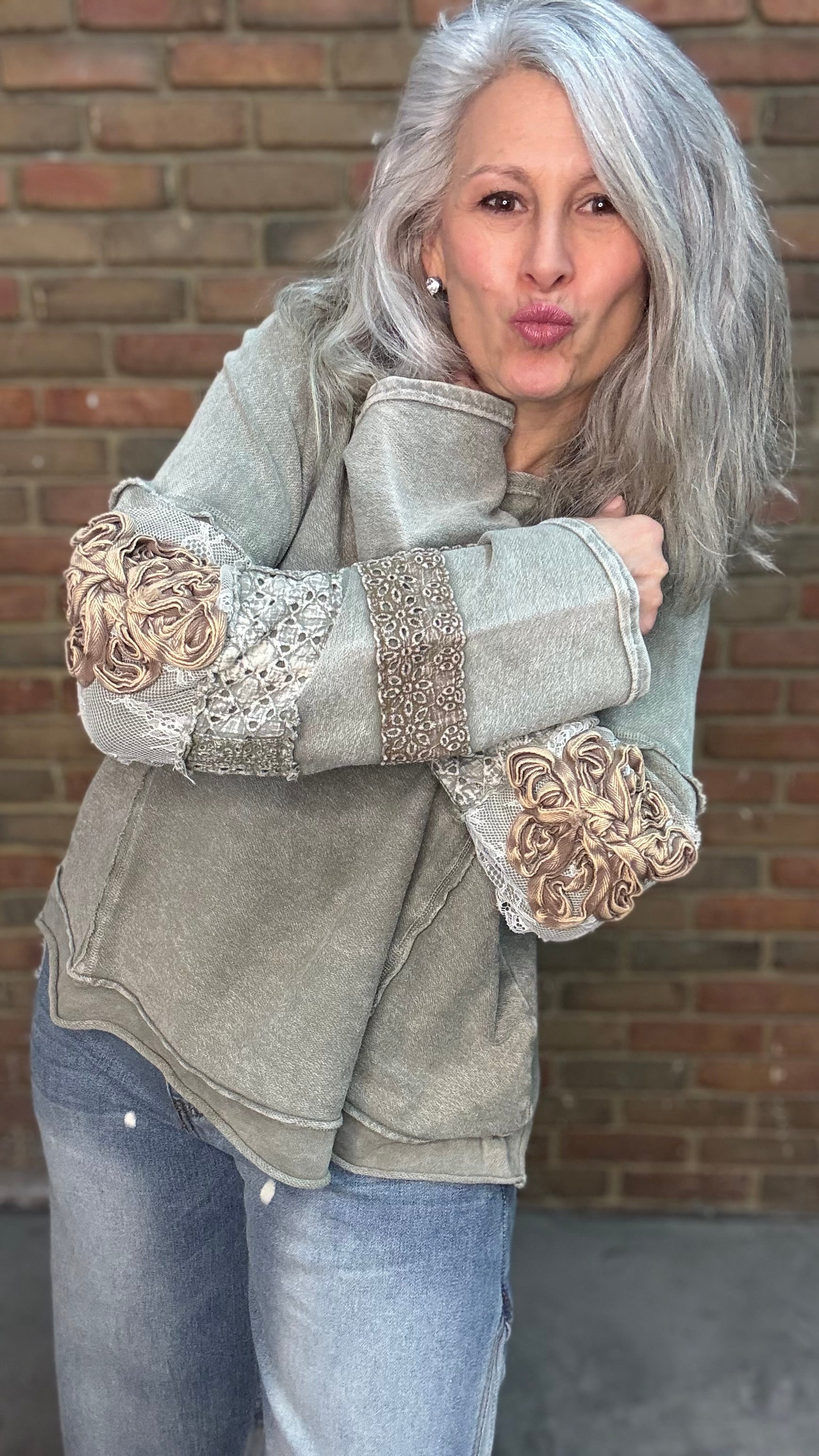 Woman wearing the Olive Embellished Sleeve Top and Bleached Wide Leg Jeans standing against a brick wall.