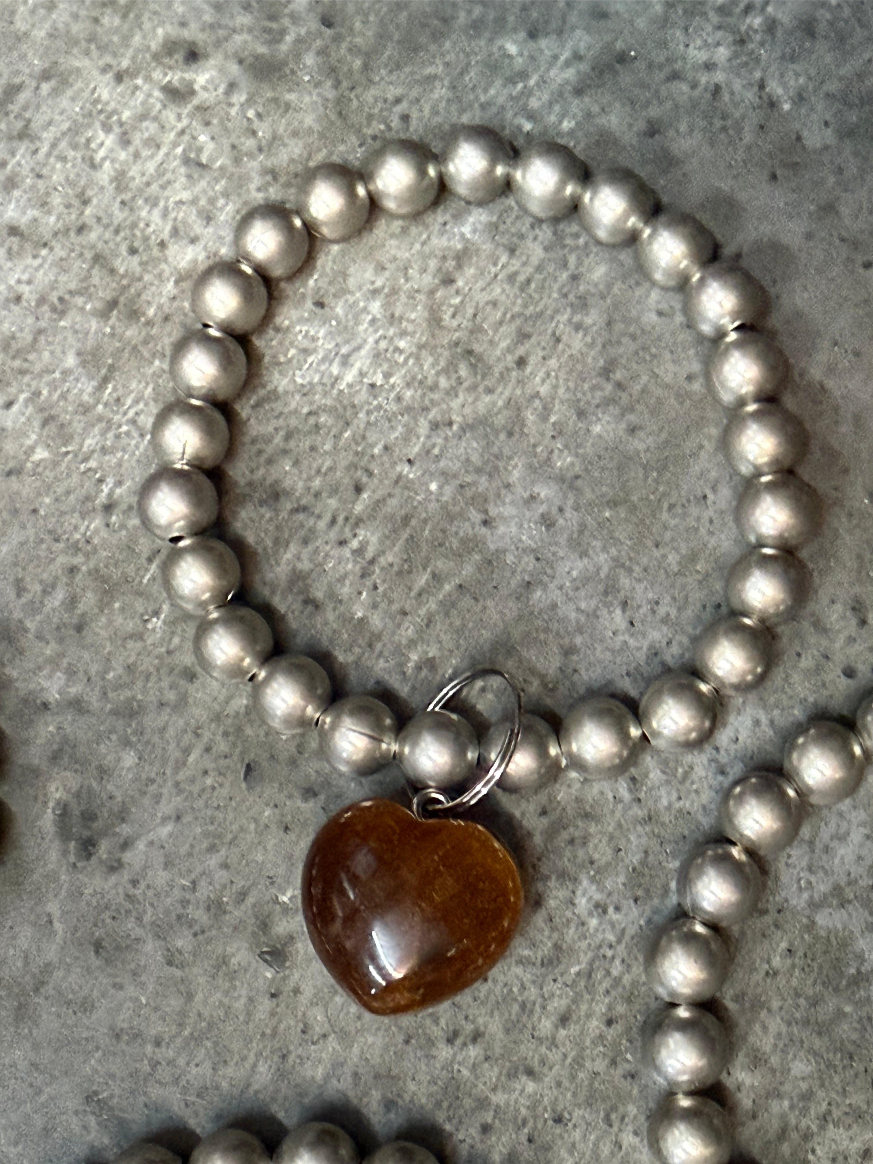 Silver beaded bracelet with a heart-shaped brown stone on a concrete surface