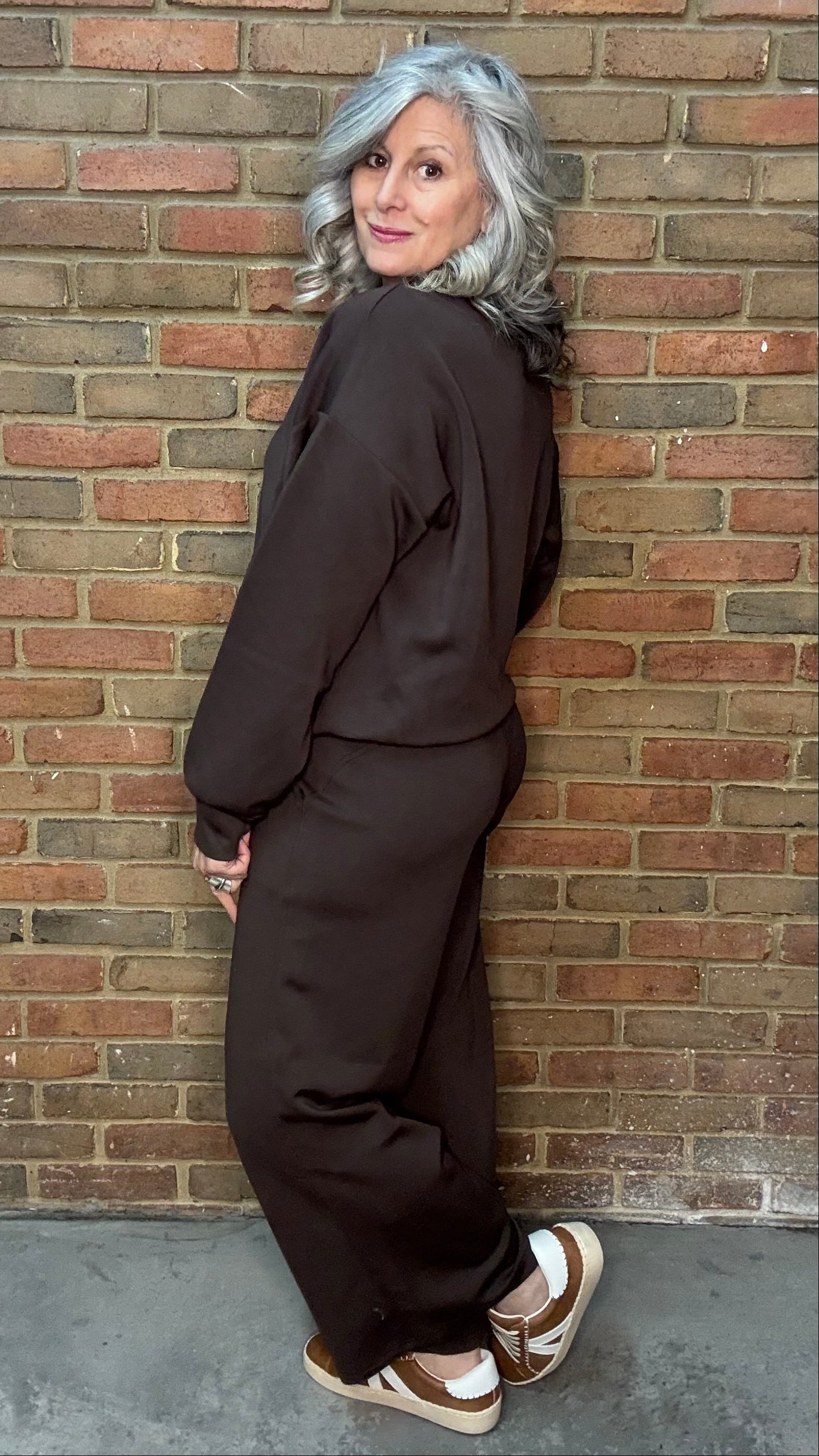 Person wearing a brown outfit leaning against a brick wall