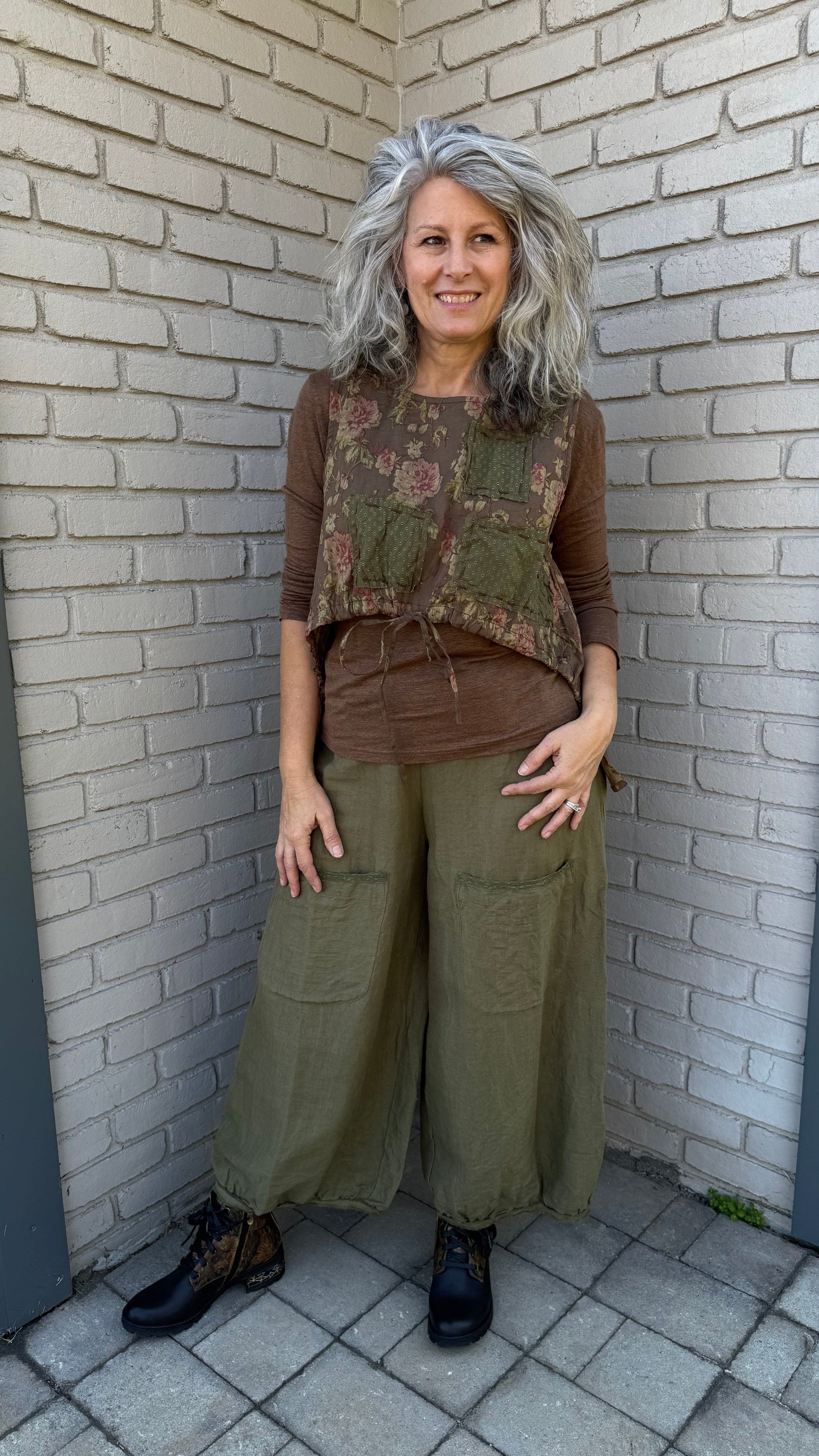 Person wearing a floral vest and green pants standing on a tiled floor.