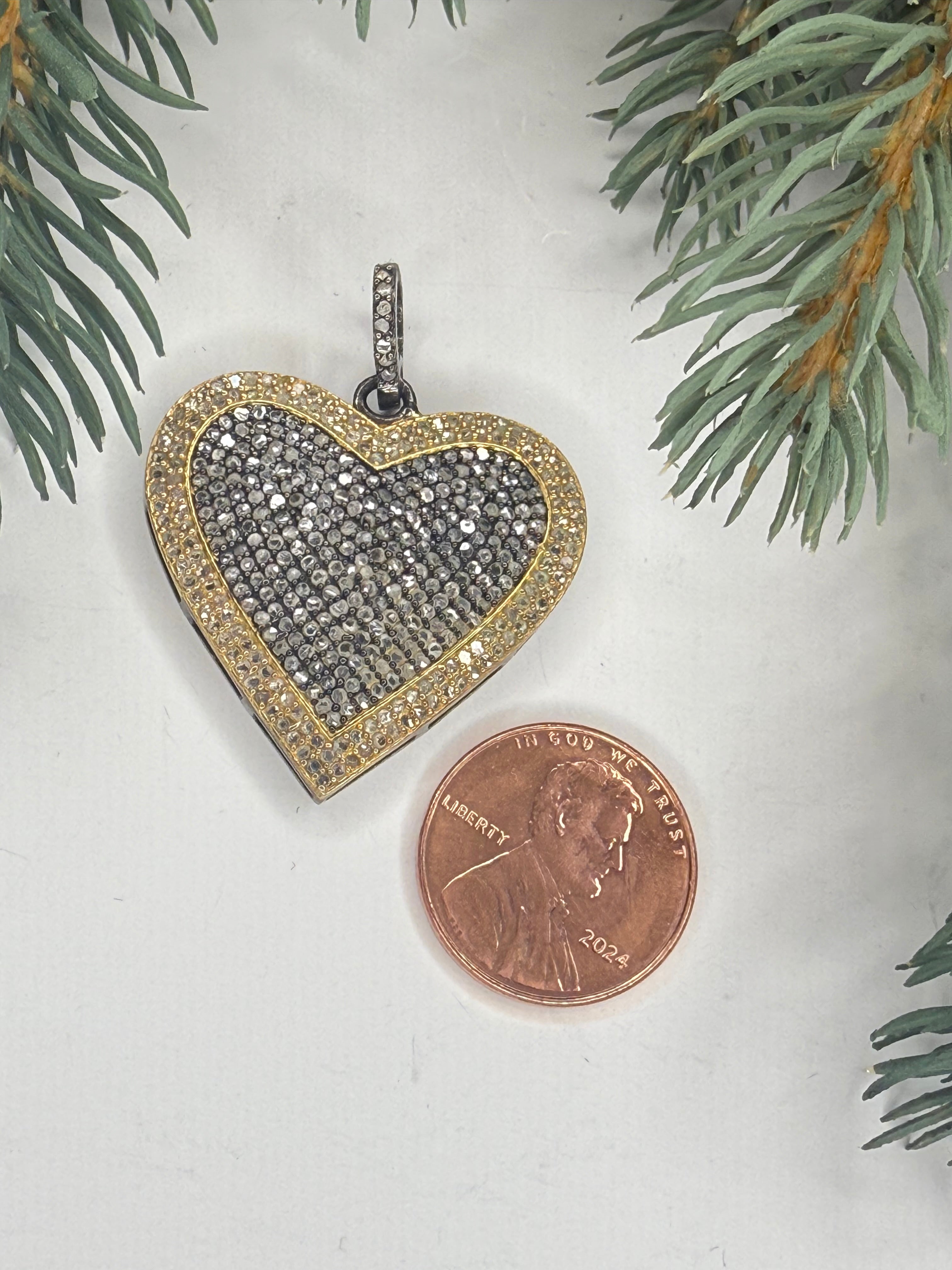 Heart-shaped pendant next to a penny on a light background with greenery.