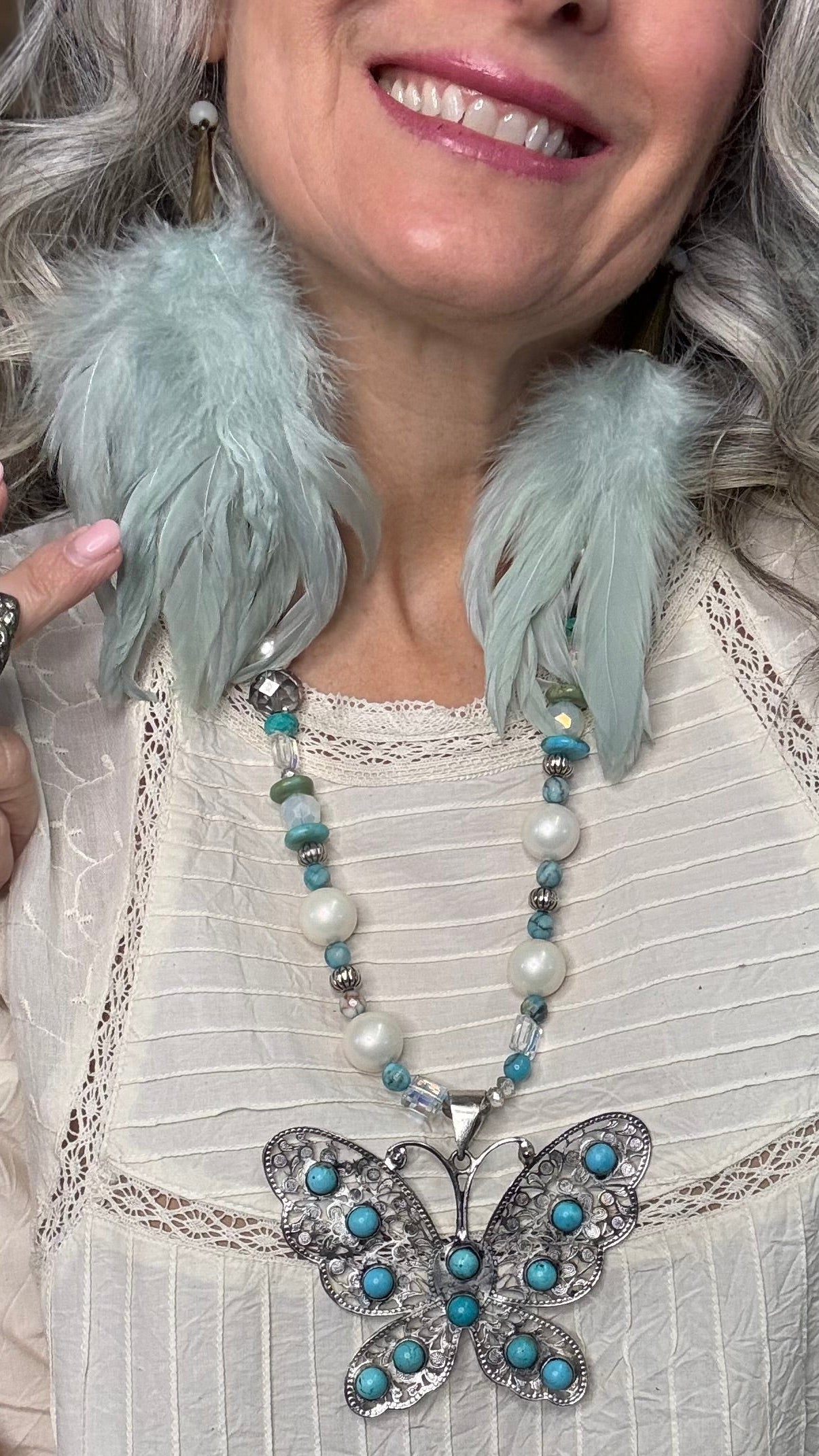 Woman wearing a straw hat with Sage Feather Earrings and a gray top against a brick wall.