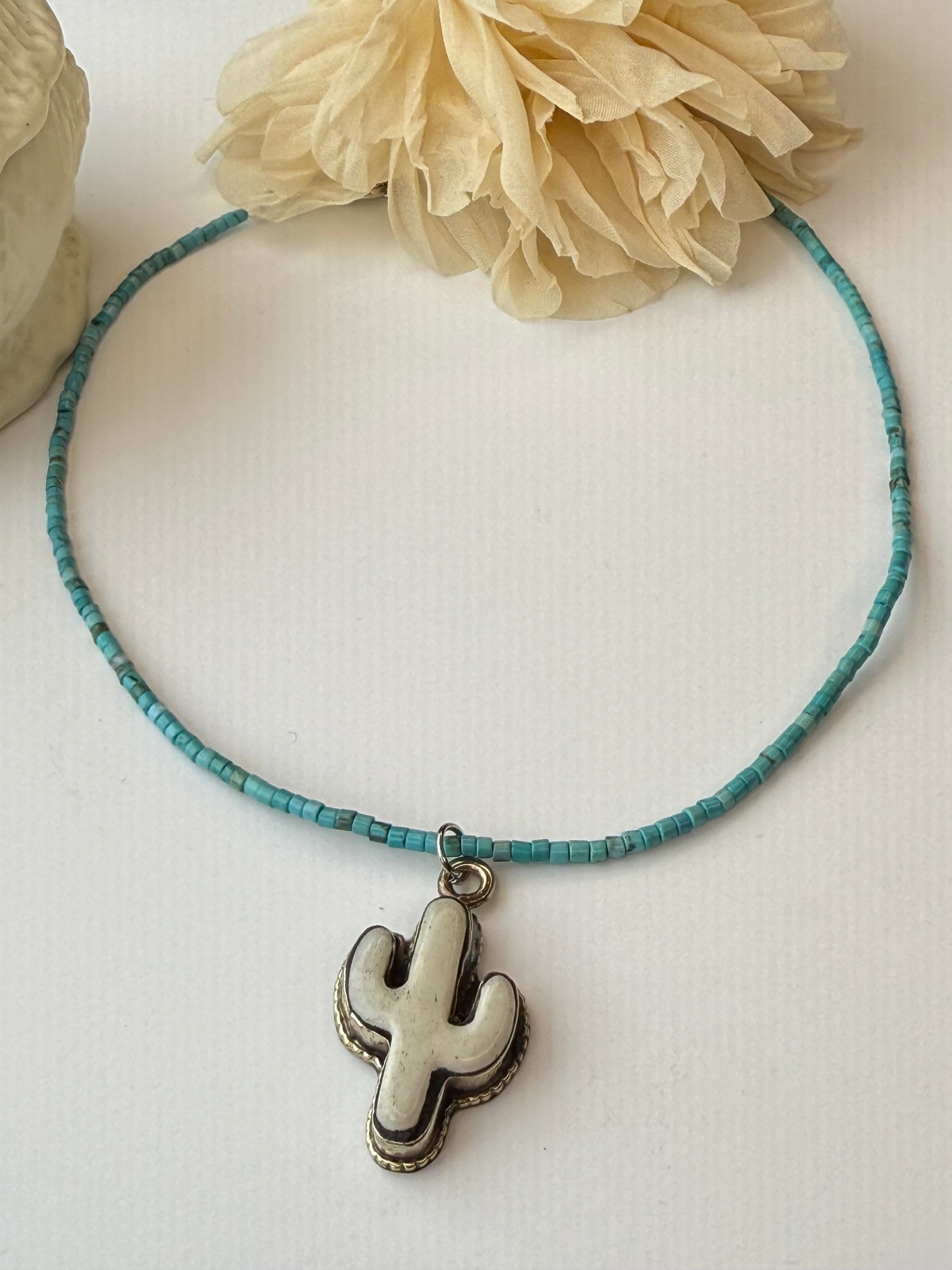 Necklace with a cactus design on a white surface with a beige flower.