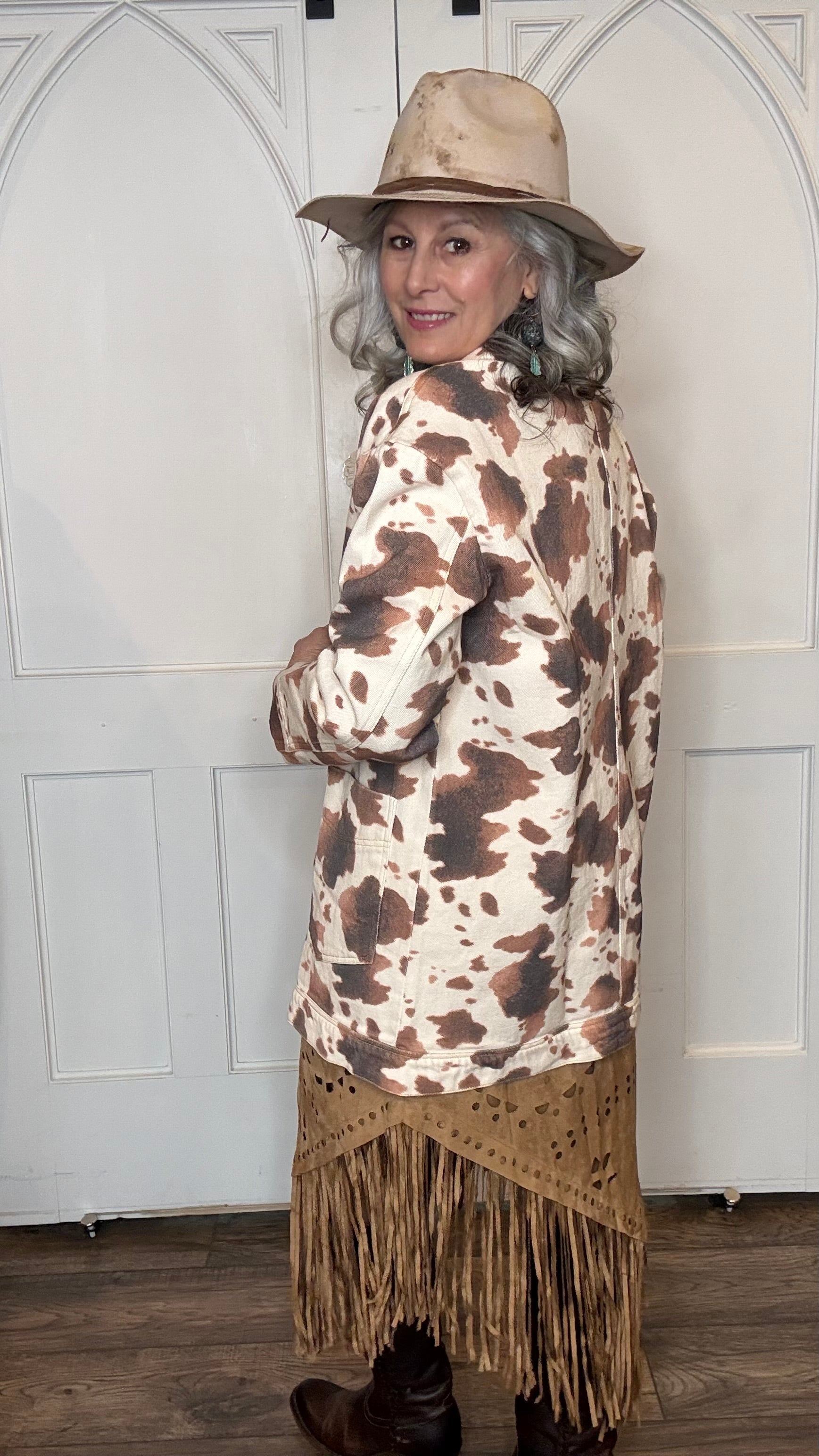 Woman wearing the Cow Print Denim Jacket, the Camel Faux Suede Fringe Skirt, topped the solid Mesh top in Brown and the Wide Triangle Buckle Belt. Shoes are the Lane Plain Jane Boots, and she is wearing the Pop&