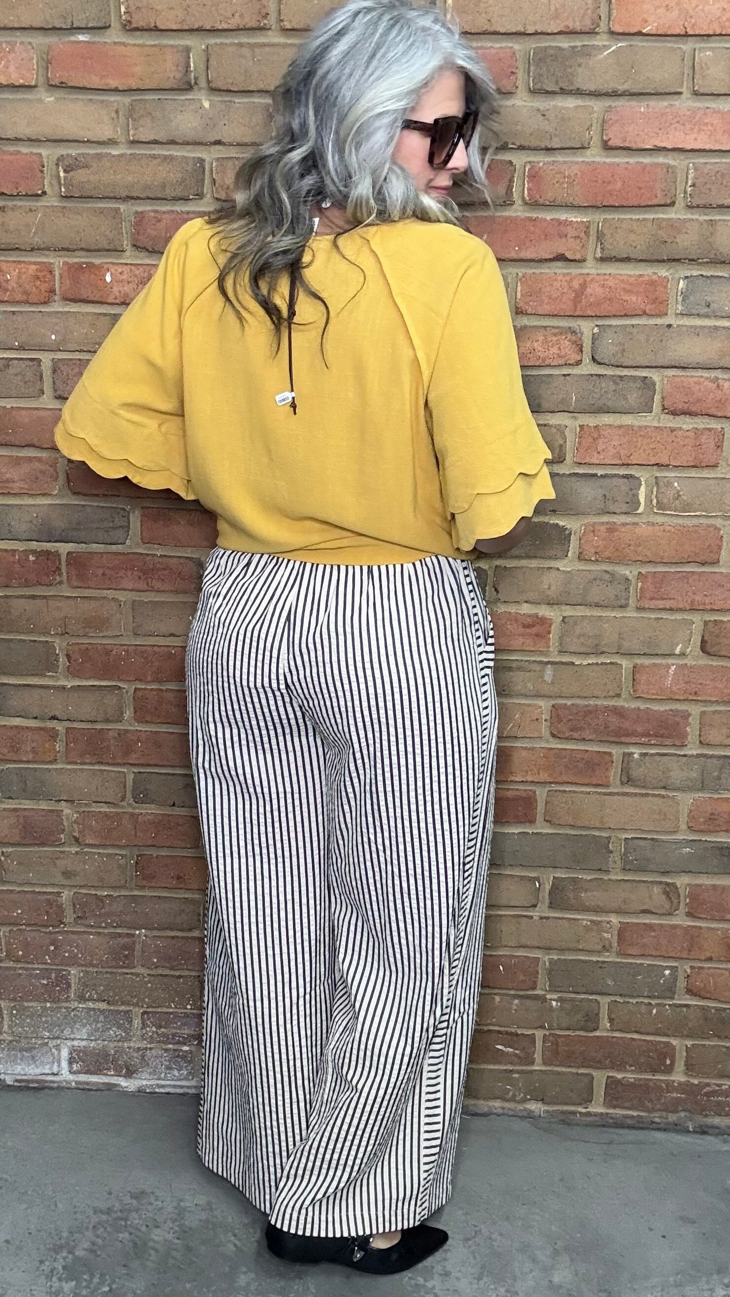 Woman in a mustard and Latte Wide Leg Pull On Pant standing against a brick wall.