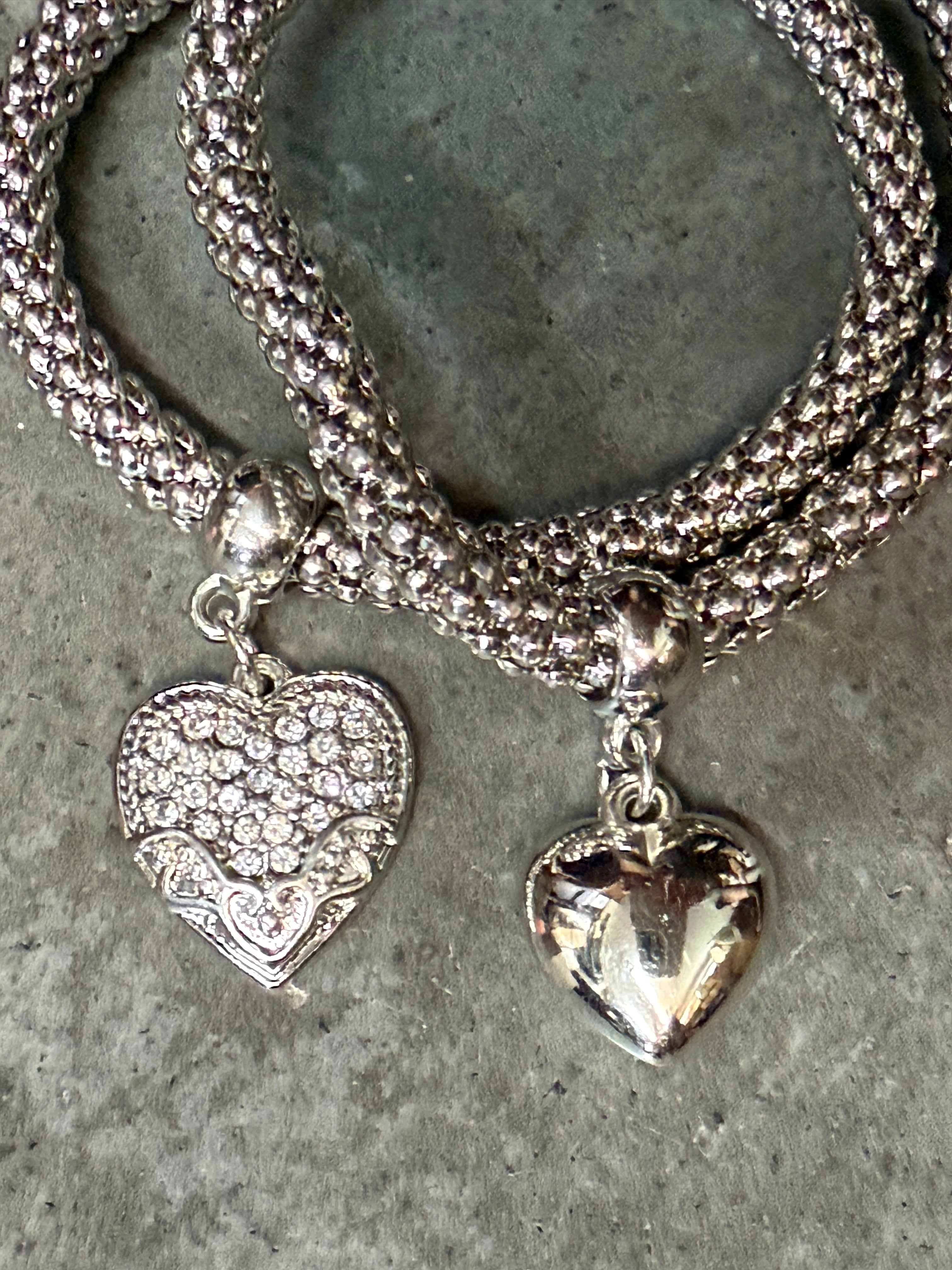 Silver bracelet with heart-shaped pendants on a concrete surface